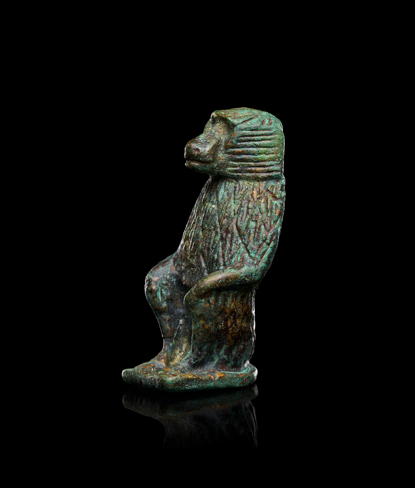 AN EGYPTIAN BRONZE BABOON LATE PERIOD, CIRCA 664-323 B.C.: AN EGYPTIAN BRONZE BABOON, LATE PERIOD, CIRCA 664-323 B.C.Modelled seated on a rectangular plinth, the figure rests with hindquarters lowered and forelimbs extended downward to the base, the hands set
