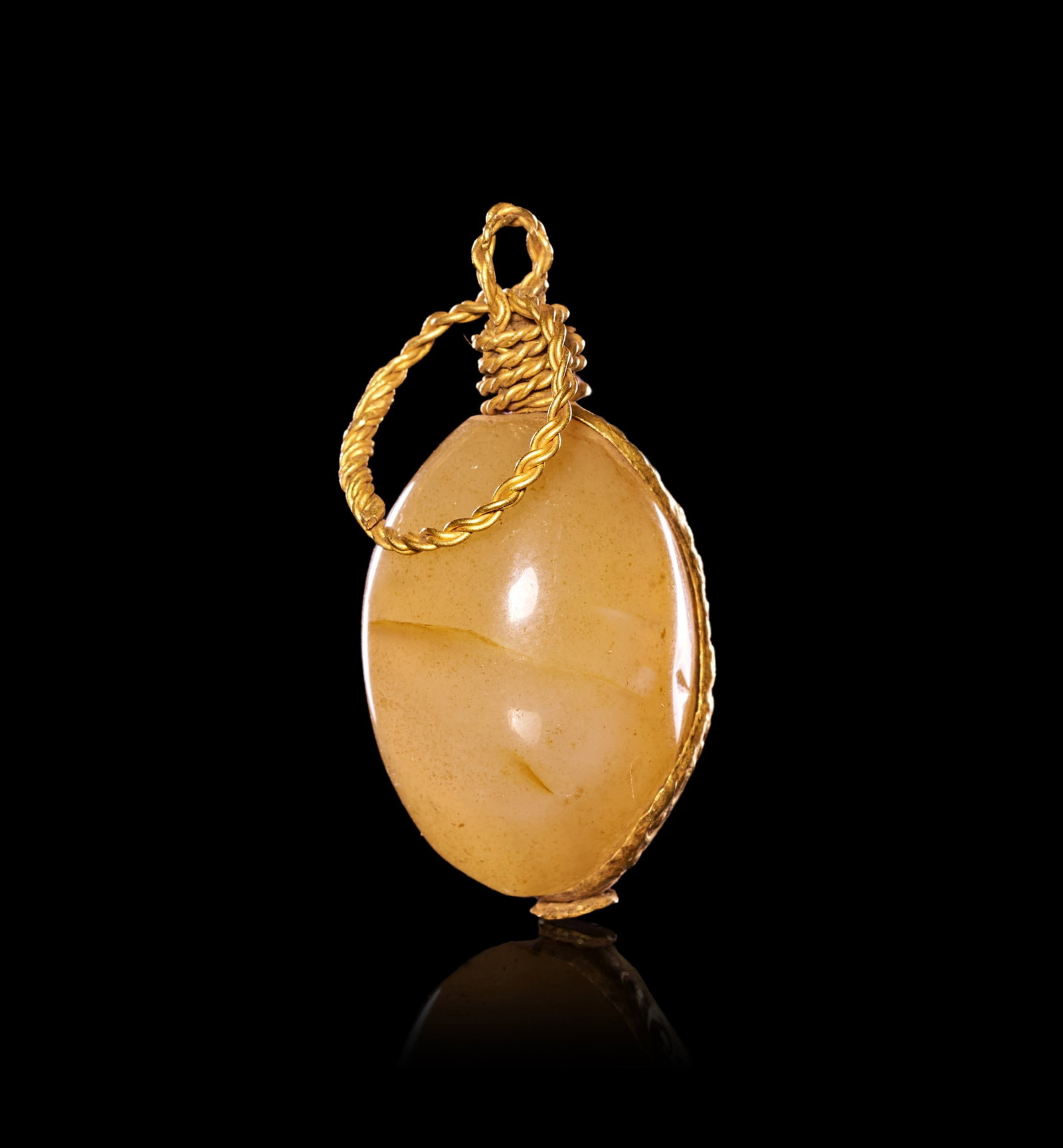 A VIKING AGATE BEAD ON A HAMMERED GOLD AMULET, CIRCA 10TH CENTURY A.D.: A VIKING AGATE BEAD ON A HAMMERED GOLD AMULET, CIRCA 10TH CENTURY A.D.Of ovoid form, the polished agate bead of warm honey tone is drilled through its long axis and mounted within a shaped sheet-gold 