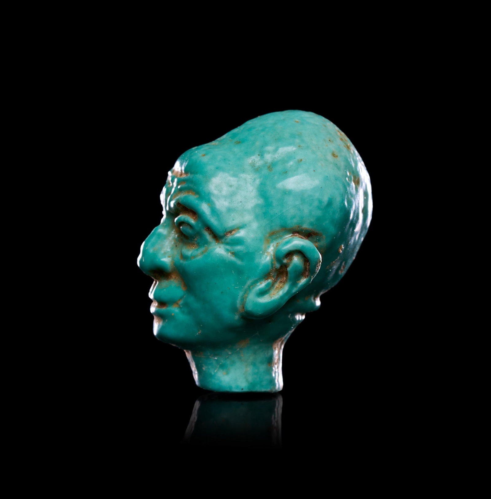 AN EGYPTIAN FAIENCE HEAD OF PTAH, NEW KINGDOM, DYNASTY XVIII, CIRCA 1353-1336 B.C.: AN EGYPTIAN FAIENCE HEAD OF PTAH, NEW KINGDOM, DYNASTY XVIII, CIRCA 1353-1336 B.C.Modelled in the round on a small rectangular tenon, the head presents a mature male face rendered with unusual natural