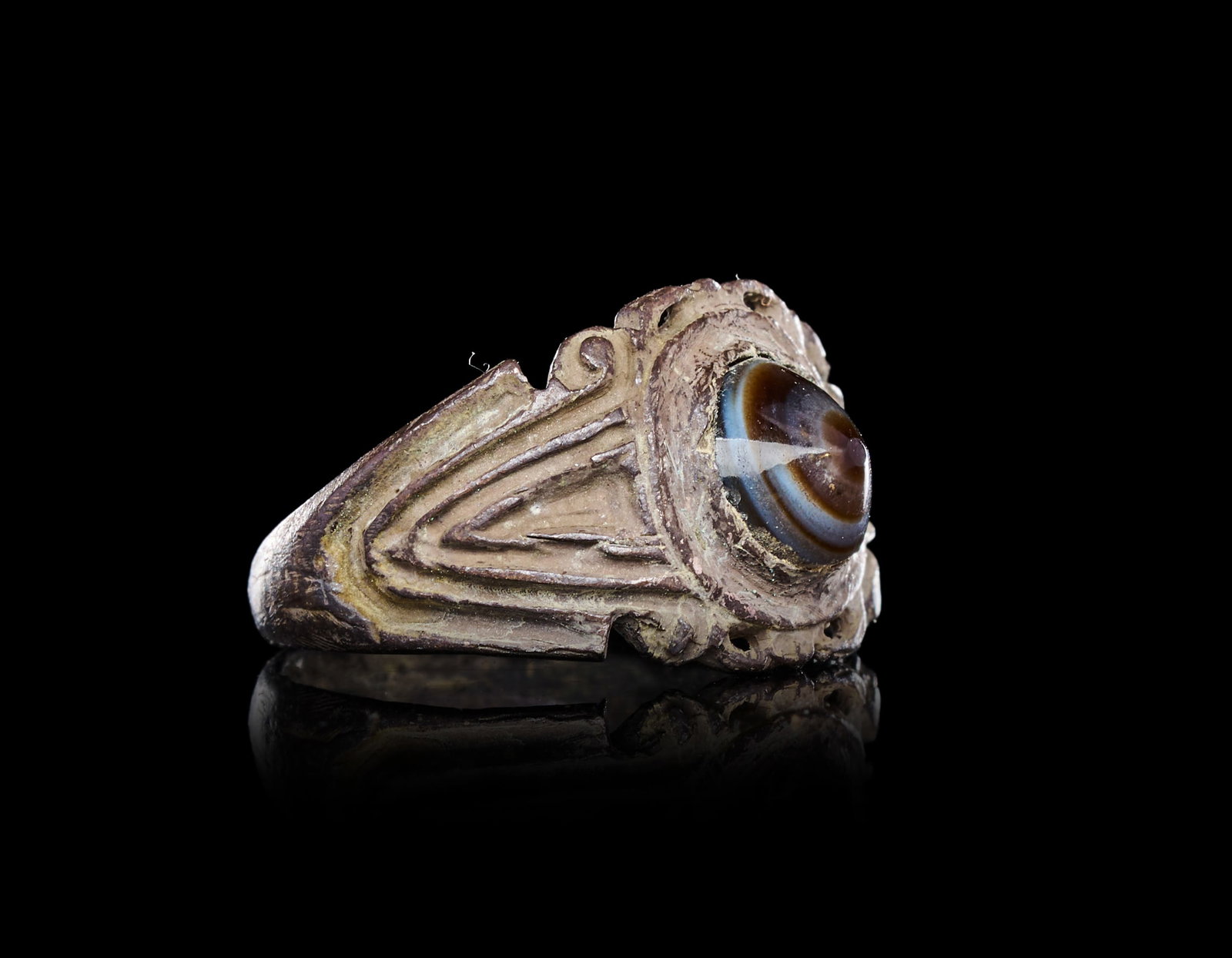 A ROMAN SILVER FINGER RING WITH AN AGATE: A ROMAN SILVER FINGER RING WITH AN AGATE "DZI" EYE BEAD, CIRCA 1ST-2ND CENTURY A.D.Of substantial form, the broad hoop expanding at the shoulders into a flattened oval bezel framed by a scalloped and 