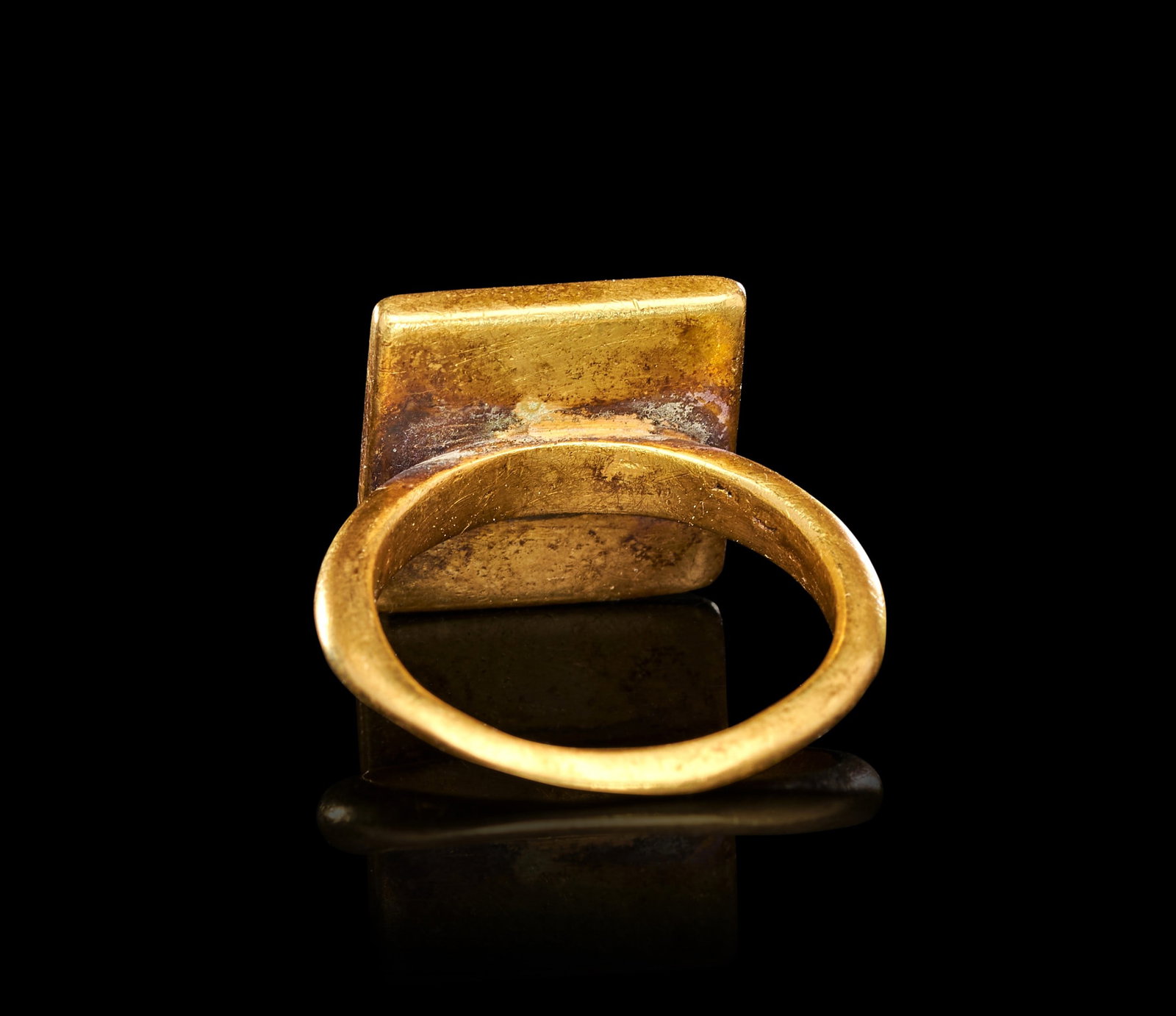 AN EGYPTIAN GOLD FINGER RING LATE PERIOD, 664-332 B.C.: AN EGYPTIAN GOLD FINGER RING, LATE PERIOD, 664-332 B.C.Of substantial construction, the plain circular hoop of solid gold expanding at the shoulders to support a large square bezel, the flat face deep