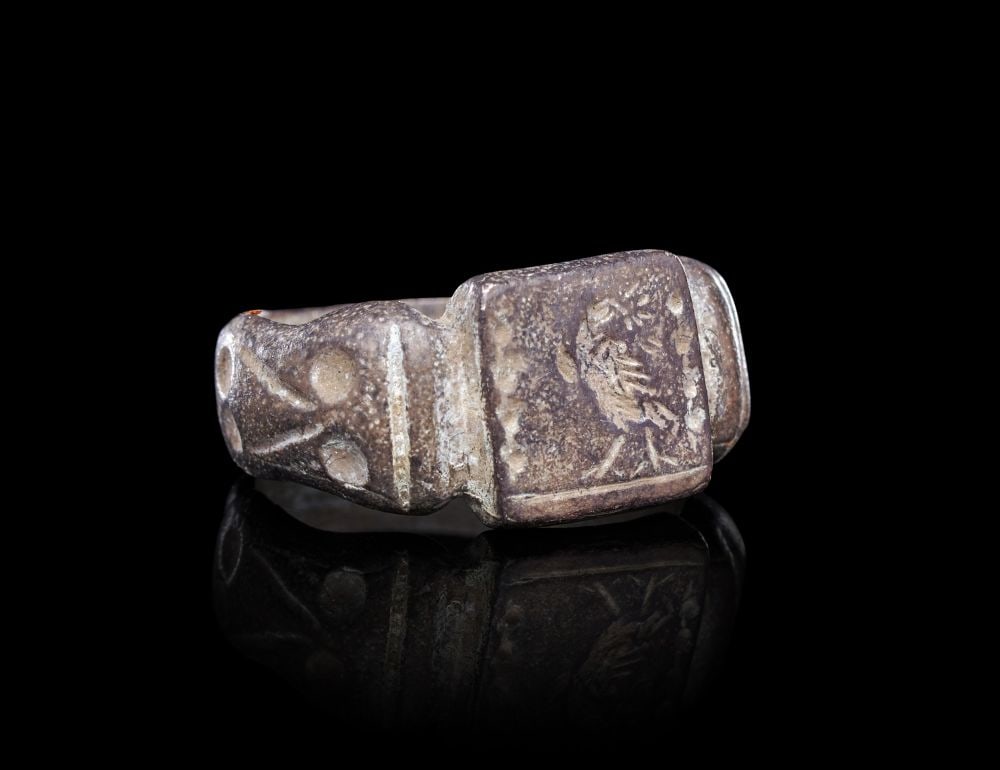 A GREEK SILVER FINGER RING ARCHAIC PERIOD, CIRCA 500 B.C.: A GREEK SILVER FINGER RING, ARCHAIC PERIOD, CIRCA 500 B.C.Of solid cast construction, the hoop of stirrup form rising from a plain interior to broad, faceted shoulders that step upward to meet a recta