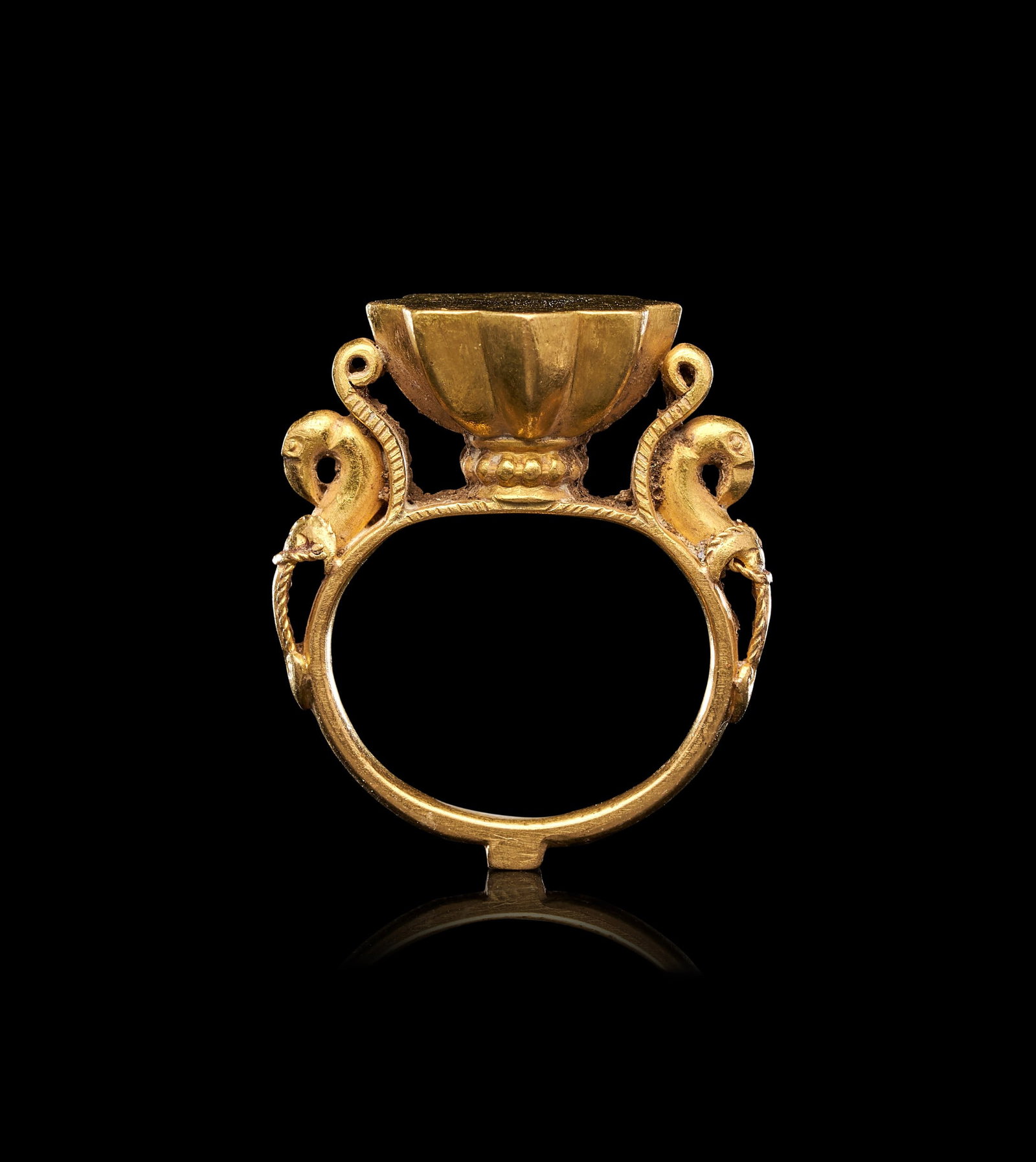 A RARE DECCAN, RING DEPICTING DEPICTING TWO BIRDS, INDIA, 17TH CENTURY, INDIA: A RARE DECCANI GOLD RING WITH CONFRONTED BIRDS, INDIA, 17TH CENTURY Of substantial form, the plain oval hoop rising to a raised bezel of deeply lobed, chalice-like profile, the underside of the bezel 