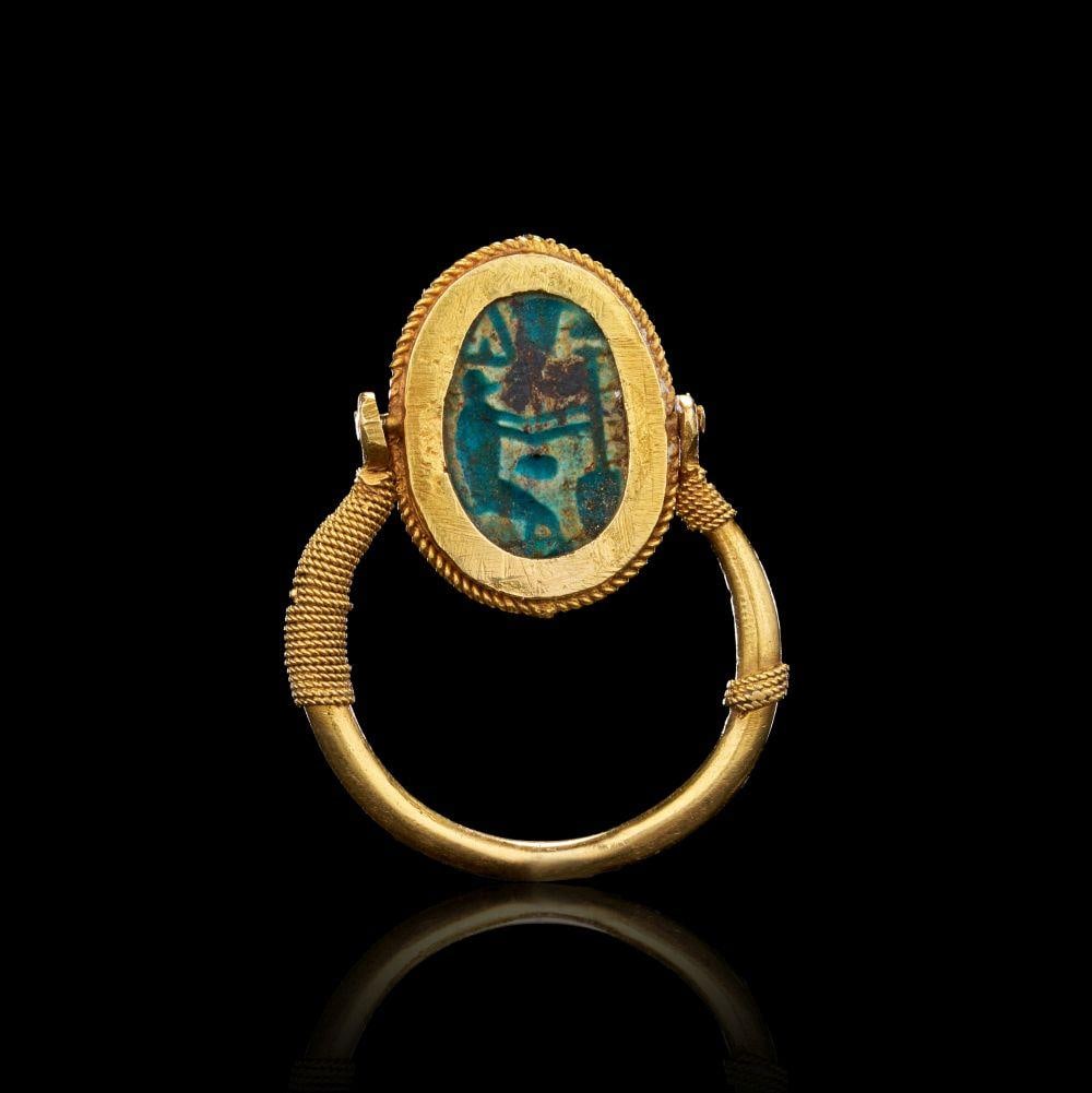 AN EGYPTIAN GOLD AND GLAZED STEATITE SCARAB SWIVEL RING New Kingdom, 19th–20th Dynasty, Circa: AN EGYPTIAN GOLD AND GLAZED STEATITE SCARAB SWIVEL RINGNew Kingdom, 19th–20th Dynasty, Circa 1279–1069 B.C.Formed in high-karat gold, this swivel ring is mounted with an oval glazed steatite scara