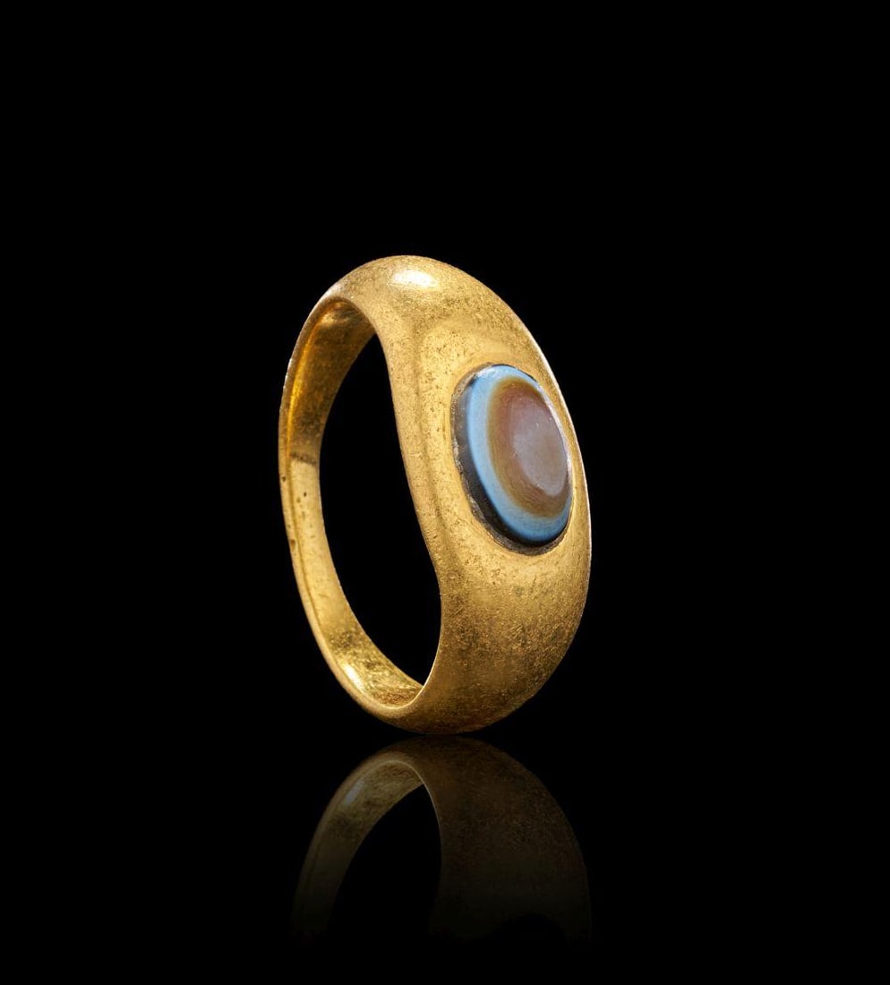 A ROMAN GOLD RING SET WITH AN AGATE ‘EYE’ BEAD Circa 1st Century A.D.: A ROMAN GOLD RING SET WITH AN AGATE ‘EYE’ BEADCirca 1st Century A.D.Formed from a smoothly rounded band of high-karat gold, the ring is set with an oval agate bead distinguished by its natural con