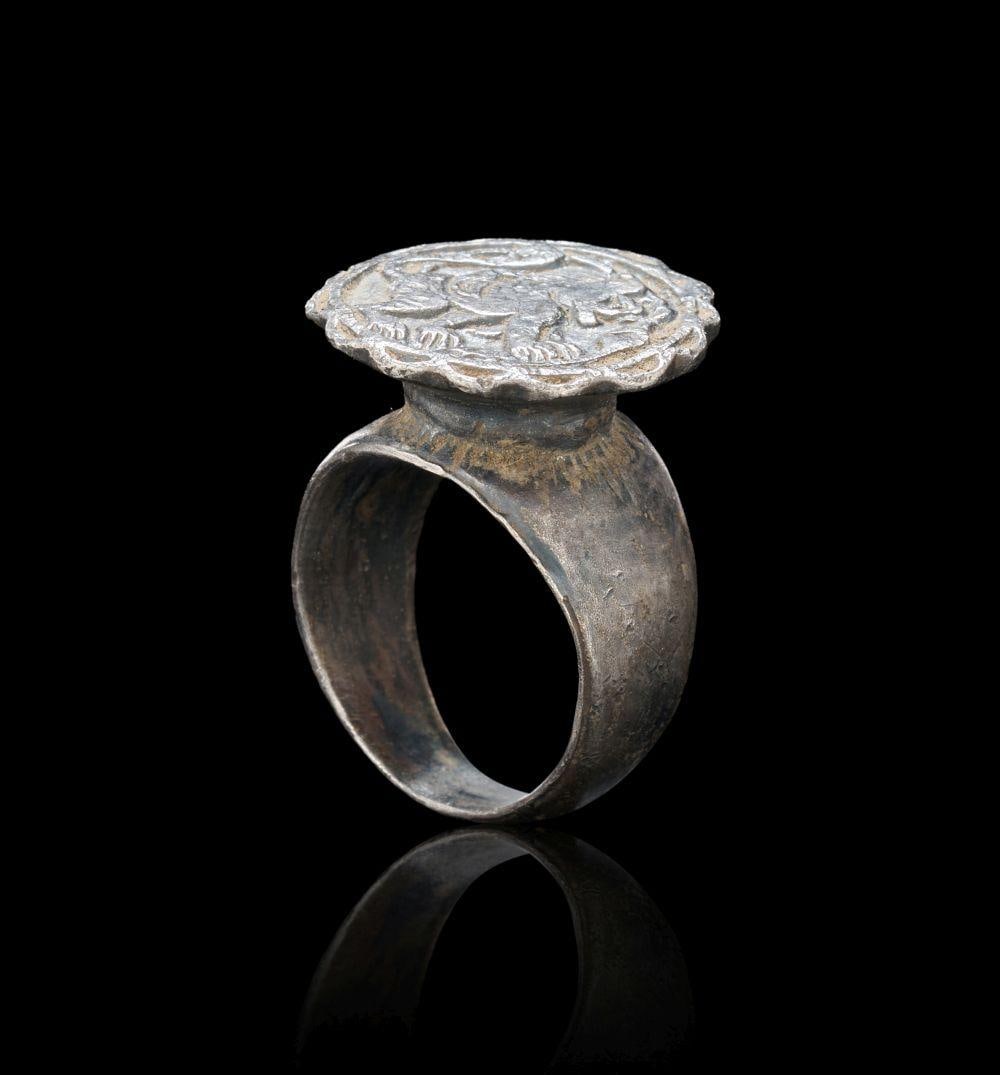 A MEDIEVAL SILVER RING DEPICTING A LION Circa 14th Century A.D.: A MEDIEVAL SILVER RING DEPICTING A LIONCirca 14th Century A.D.Cast in silver, this ring features a large, round bezel with a scalloped outer edge and a raised intaglio-style design of a lion in profil
