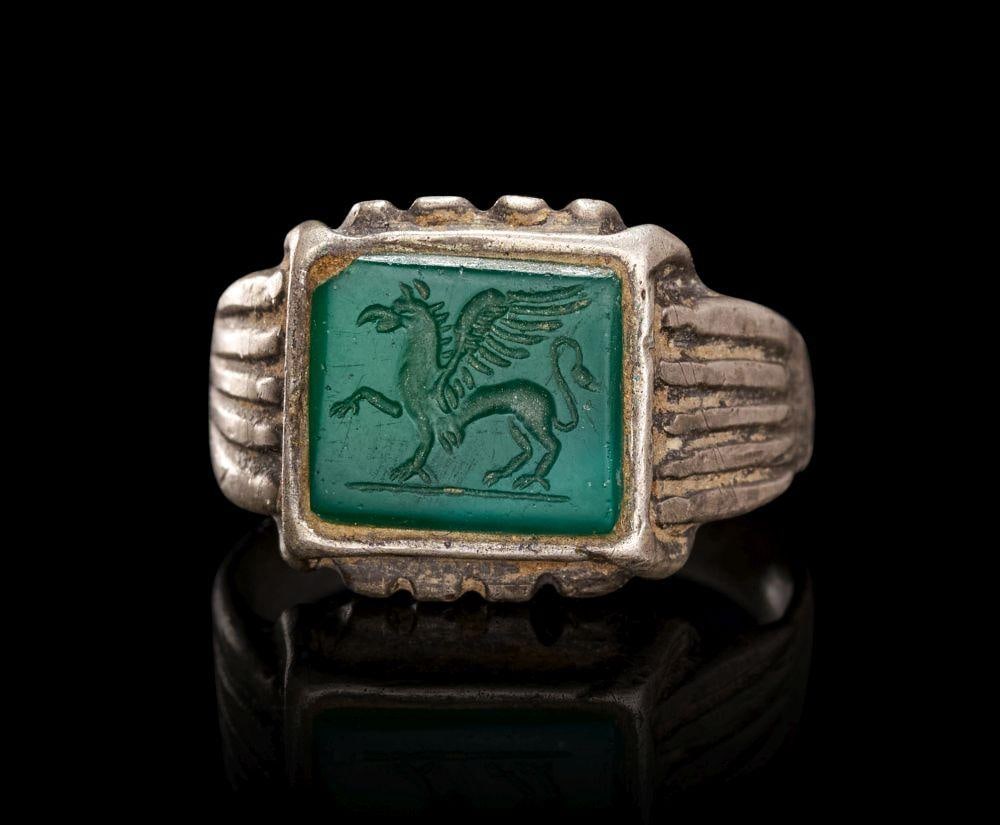 A MEDIEVAL SILVER RING WITH AN ENGRAVED SPHINX INTAGLIO, CIRCA 14TH CENTURY: A MEDIEVAL SILVER RING WITH AN ENGRAVED SPHINX INTAGLIO, CIRCA 14TH CENTURYOf substantial form, the silver hoop rising from ribbed, fluted shoulders to a rectangular bezel with crenellated upper and l
