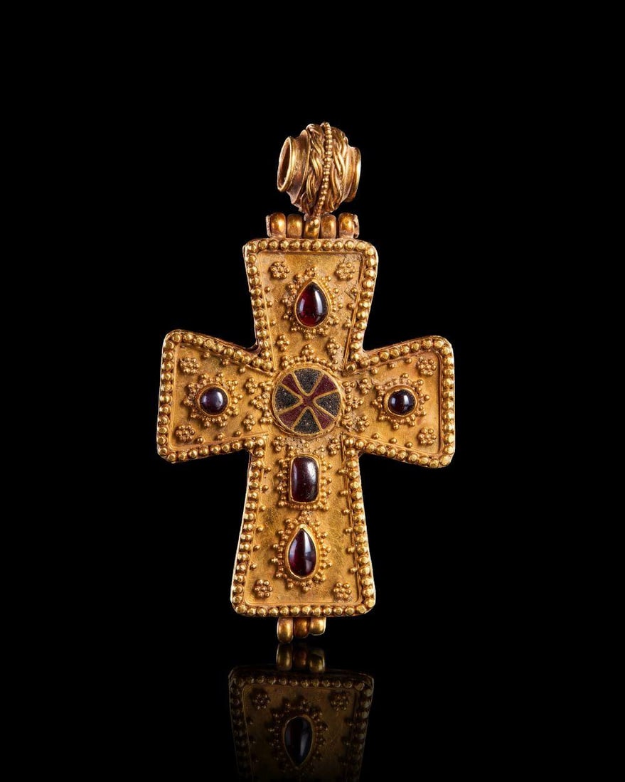 A BYZANTINE GOLD & GEM CROSS, CIRCA 7TH CENTURY: A BYZANTINE GOLD & GEM CROSS, CIRCA 7TH CENTURY Composed of high-karat gold, this cross-shaped pendant is elaborately decorated with applied filigree granulation and beaded edging. The face is set wit