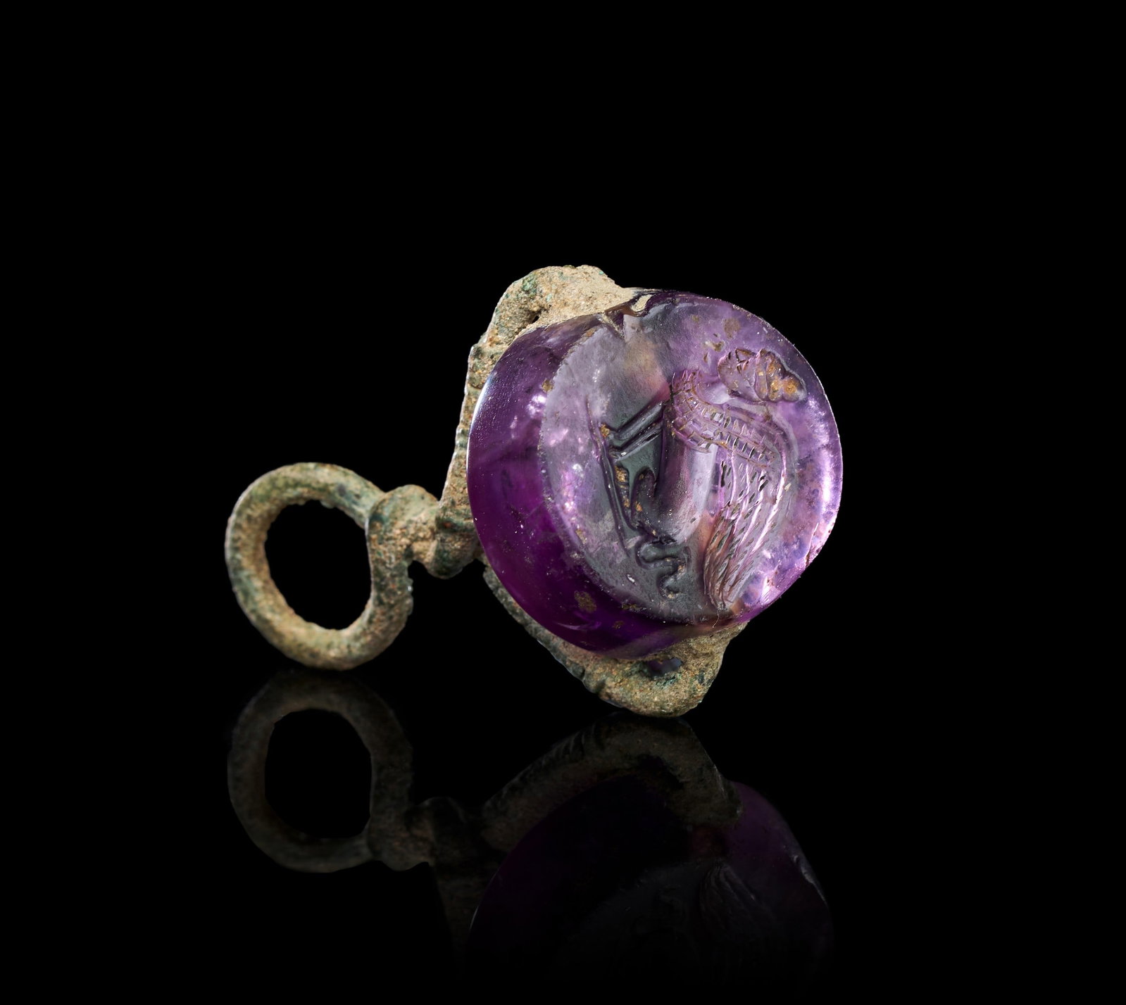 A GREEK AMETHYST SCARABOID INTAGLIO OF A SPHINX SET IN A BRONZE SWIVEL, CIRCA 4TH-3RD CENTURY B.C.: A GREEK AMETHYST SCARABOID INTAGLIO OF A SPHINX SET IN A BRONZE SWIVEL, CIRCA 4TH-3RD CENTURY B.C. The domed amethyst scaraboid is set transversely within a corroded bronze swivel mount, the hoop term