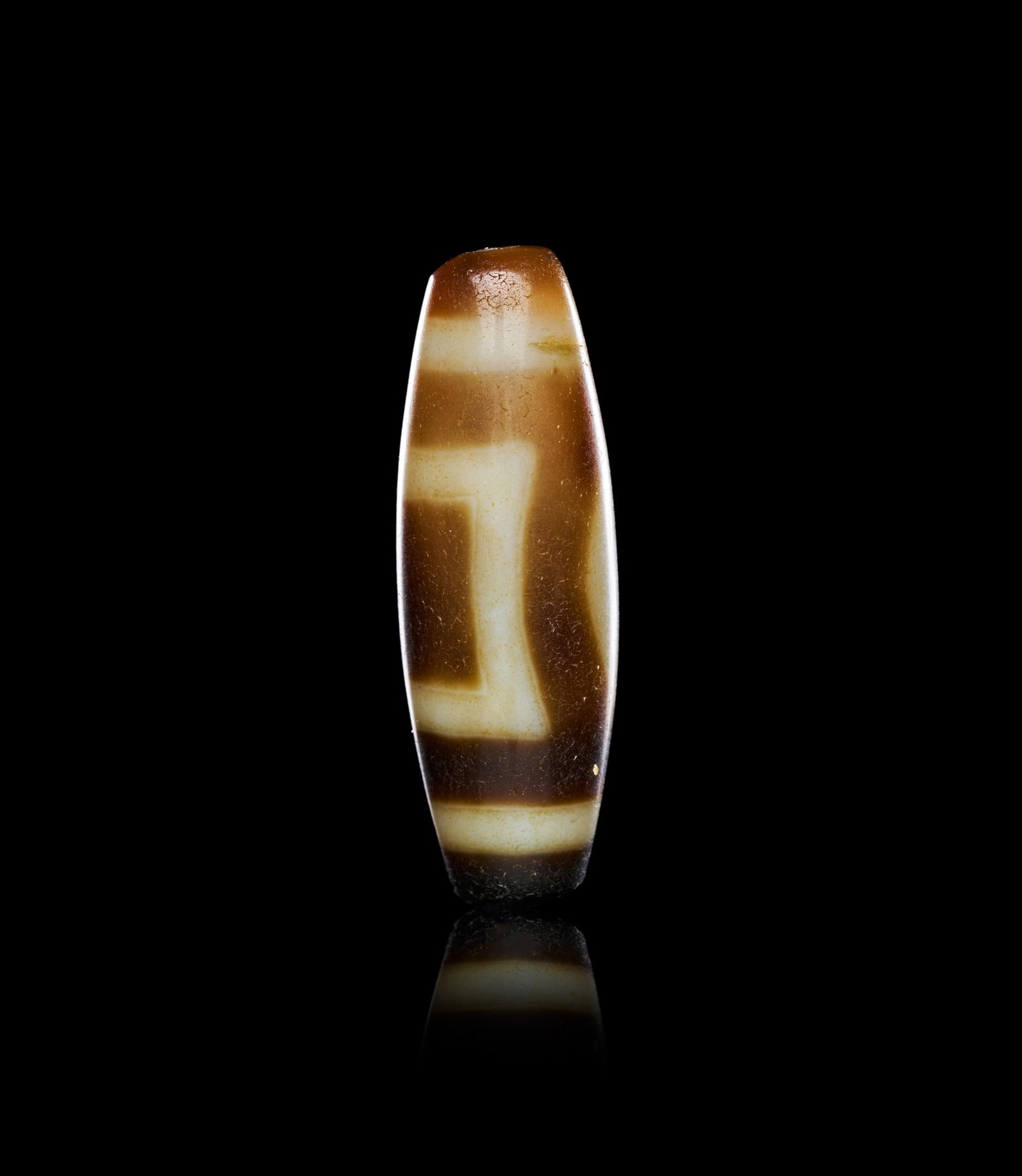 AGATE: AN AGATE "DZI" EYE BEAD, CIRCA 1ST-2ND CENTURY A.D.Of elongated barrel form, tapering gently toward each terminal and pierced longitudinally for suspension, the bead worked from a banded agate of warm