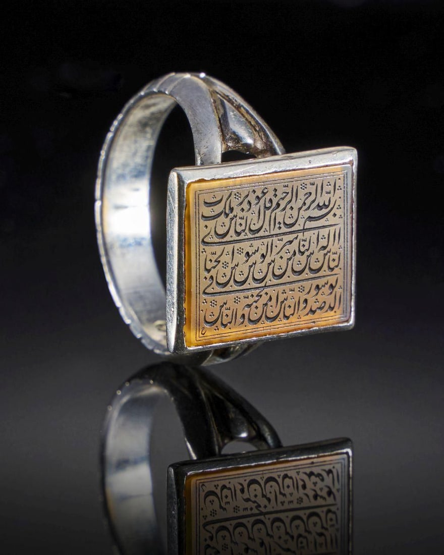 A CALLIGRAPHIC INSCRIBED AGATE RING ON SILVER, 19TH CENTURY, PERSIA: A CALLIGRAPHIC INSCRIBED AGATE RING ON SILVER, 19TH CENTURY, PERSIA This intricate 19th-century Persian ring features an oval agate stone, meticulously inscribed with intricate calligraphy. The agate,