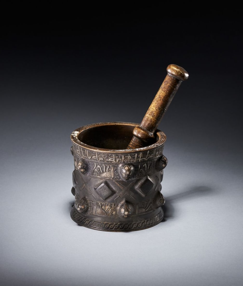 A SILVER INLAID SELJUK MORTAR, 12TH CENTURY, PERSIA: A SELJUK SILVER-INLAID BRONZE MORTAR AND PESTLE, PERSIA, 12TH CENTURY Of cylindrical form, the slightly waisted body rising from a spreading foot to a thickened everted rim, cast in bronze and divided