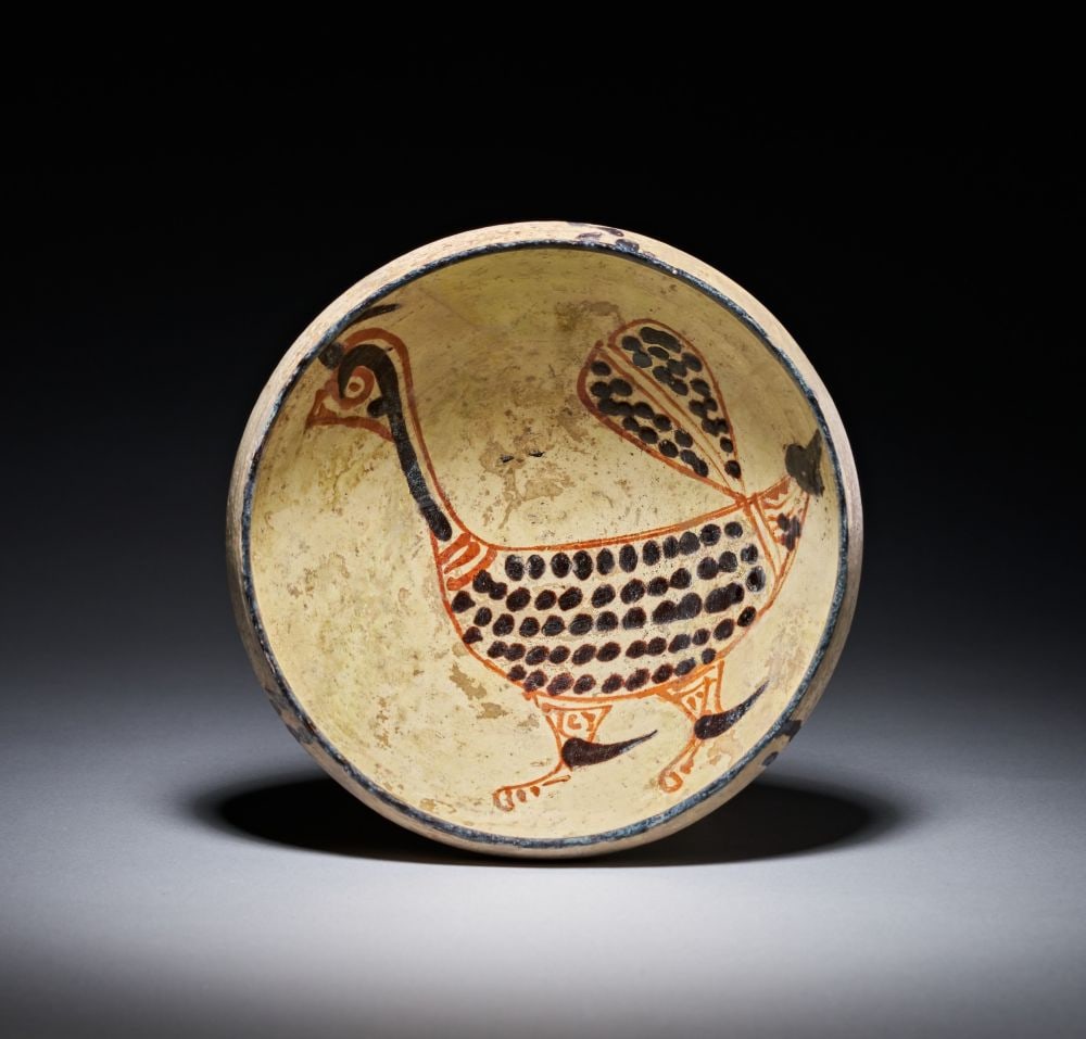 A NISHAPUR POTTERY BOWL WITH BIRD, IRAN, 10TH CENTURY: A NISHAPUR POTTERY BOWL WITH BIRD, IRAN, 10TH CENTURY Of rounded conical form on a low foot, the interior covered in a cream slip and painted in iron-black and tomato-red with a large bird occupying n