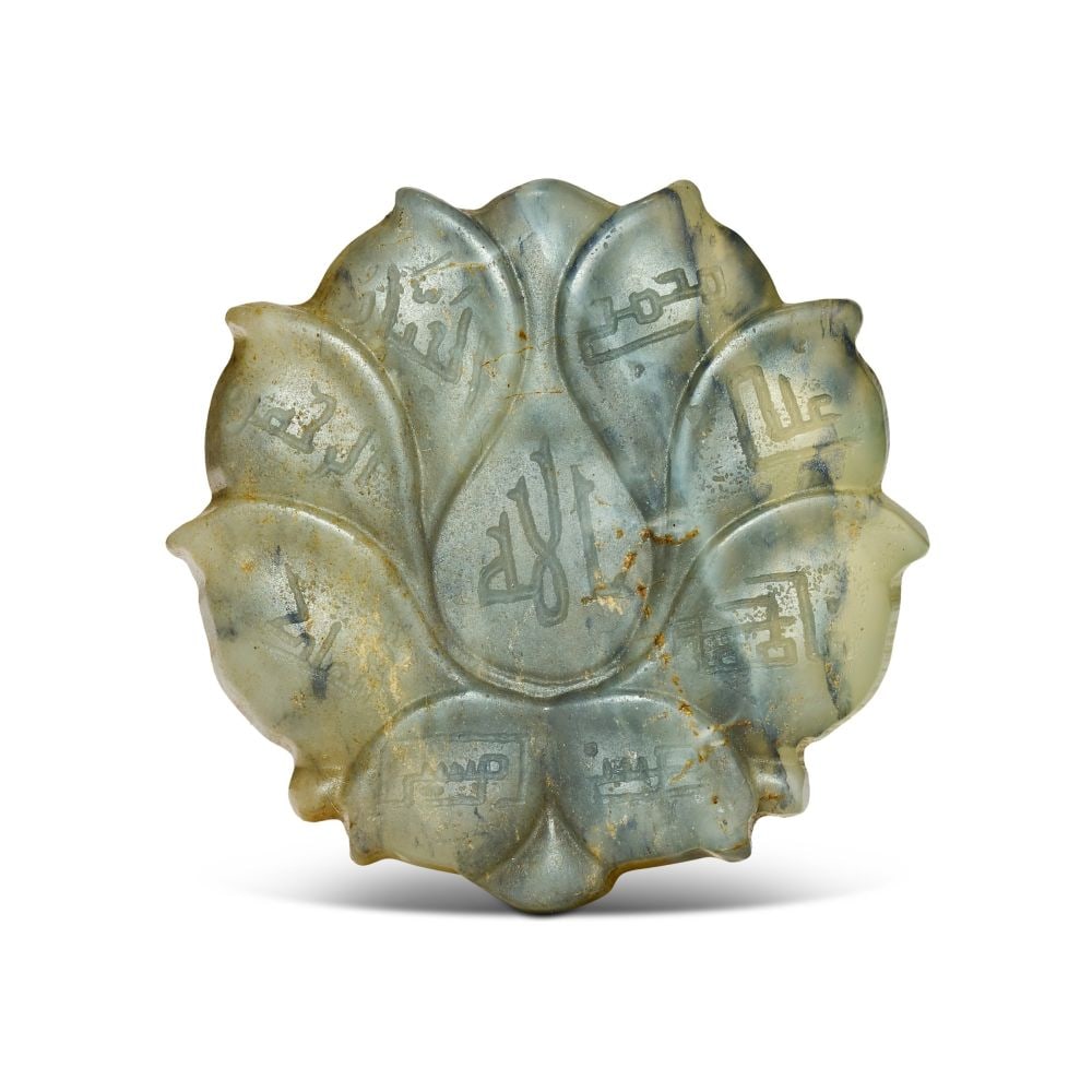 A KUFIC INSCRIBED JADE TALISMANIC AMULET, 19TH CENTURY, PERSIA: A KUFIC-INSCRIBED JADE TALISMANIC AMULET, PERSIA, 19TH CENTURY Of lobed lotiform shape, carved from a pale celadon-toned jade with natural russet and grey-blue inclusions running through the stone, th