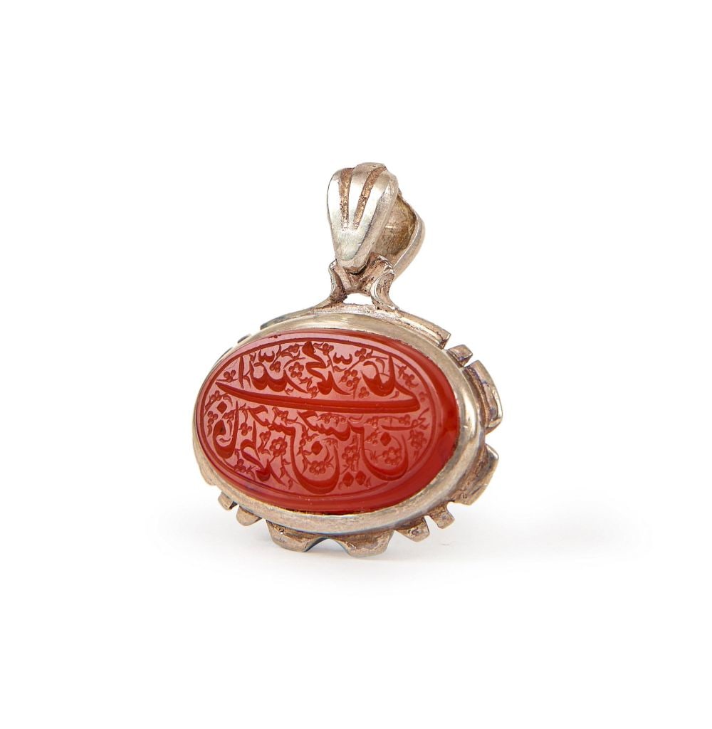A CALLIGRAPHIC INSCRIBED AGATE SEAL ON SILVER, 19TH CENTURY, PERSIA: A CALLIGRAPHIC INSCRIBED AGATE SEAL ON SILVER, 19TH CENTURY, PERSIA Of oval form, the deep orange-red agate cabochon set within a silver mount with a ribbed and toothed bezel rising to a fluted suspen