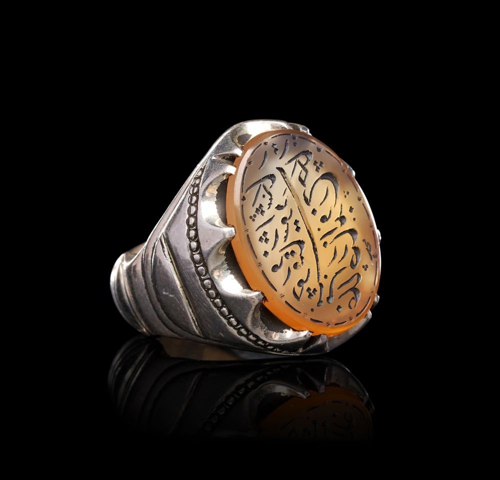 A CALLIGRAPHIC INSCRIBED AGATE RING ON SILVER, 19TH CENTURY, PERSIA: A CALLIGRAPHIC INSCRIBED AGATE RING ON SILVER, PERSIA, 19TH CENTURY Of substantial form, the heavy silver hoop rising to broad shoulders flanked by ridged and beaded mouldings, supporting a tall claw-