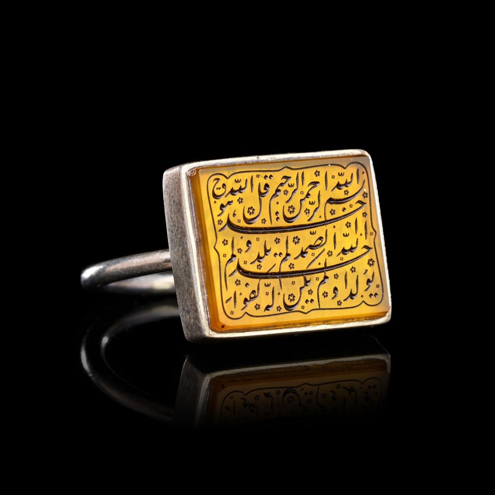 A CALLIGRAPHIC INSCRIBED AGATE RING ON SILVER, 19TH CENTURY, PERSIA: A CALLIGRAPHIC INSCRIBED AGATE RING ON SILVER, PERSIA, 19TH CENTURY The ring of plain silver construction, the slender circular hoop rising to a rectangular bezel set with a translucent honey-yellow a