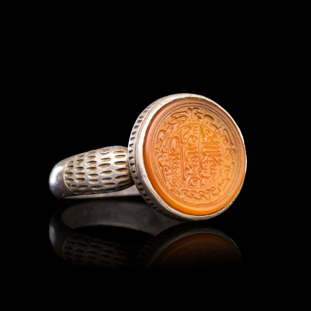 A CALLIGRAPHIC INSCRIBED AGATE RING ON SILVER, 19TH CENTURY, PERSIA: A CALLIGRAPHIC INSCRIBED AGATE RING ON SILVER, PERSIA, 19TH CENTURY The ring of substantial form, the silver hoop expanding from a plain rounded back through broad shoulders worked in a dense field of