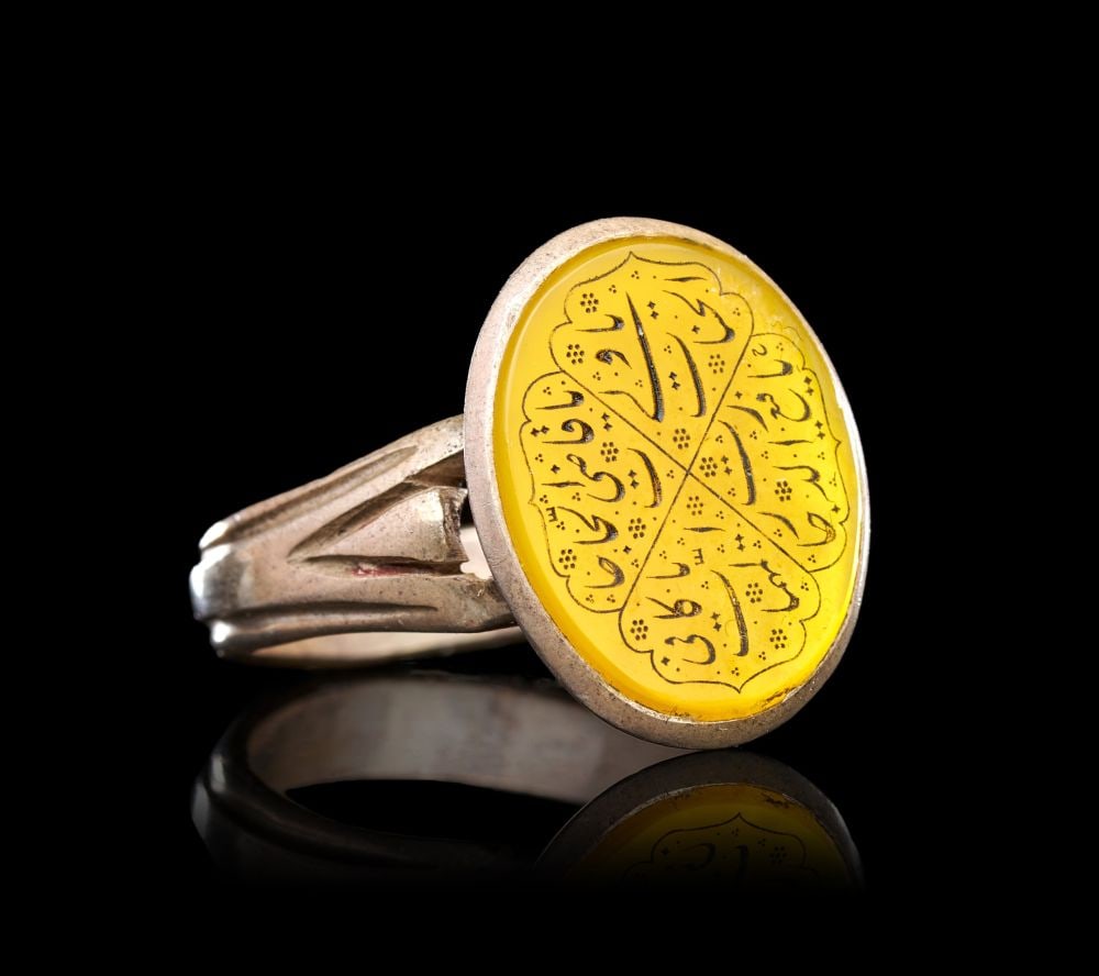 A CALLIGRAPHIC INSCRIBED AGATE RING ON SILVER, 19TH CENTURY, PERSIA: A CALLIGRAPHIC INSCRIBED AGATE RING ON SILVER, PERSIA, 19TH CENTURY The ring of substantial form, the openwork shoulders rising in pierced scrolling brackets to support a broad oval bezel, the latter 