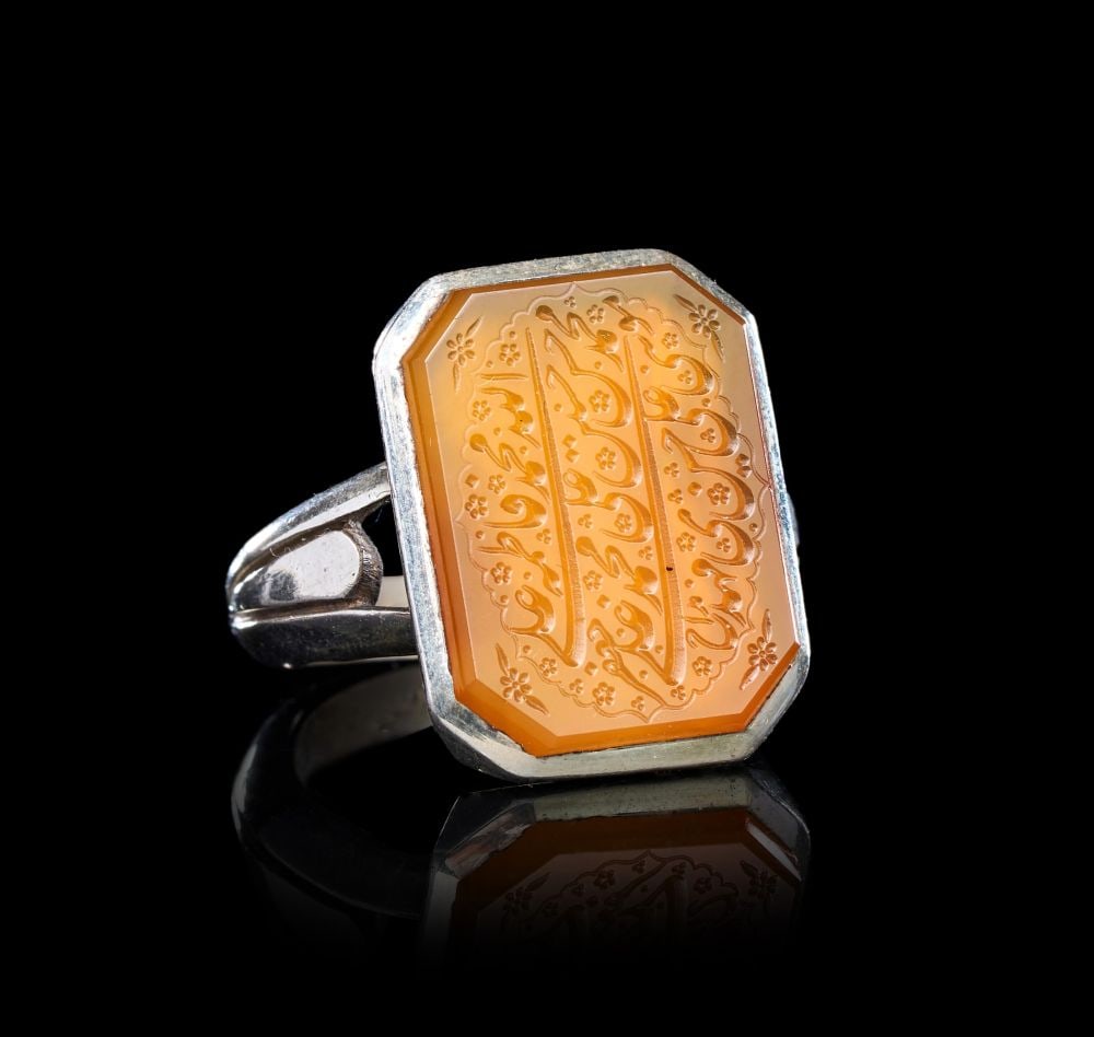 A CALLIGRAPHIC INSCRIBED AGATE RING ON SILVER, 19TH CENTURY, PERSIA: A CALLIGRAPHIC INSCRIBED AGATE RING ON SILVER, PERSIA, 19TH CENTURY The ring set with a large rectangular agate bezel of warm honey tone, the corners cut to form a chamfered octagonal field, mounted i