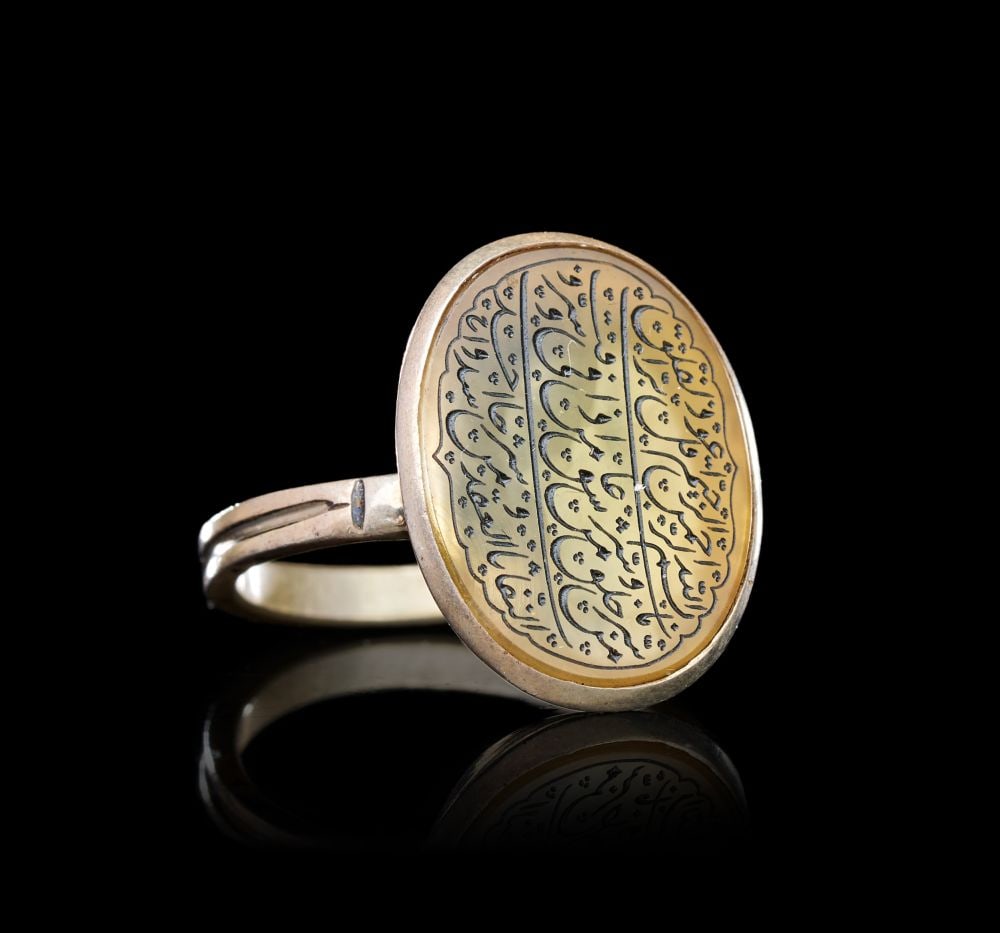 A CALLIGRAPHIC INSCRIBED AGATE RING ON SILVER, 19TH CENTURY, PERSIA: A CALLIGRAPHIC INSCRIBED AGATE RING ON SILVER, PERSIA, 19TH CENTURY Of oval form, the large pale honey-coloured agate bezel set within a plain silver collet raised on a slender double-shank hoop. The 