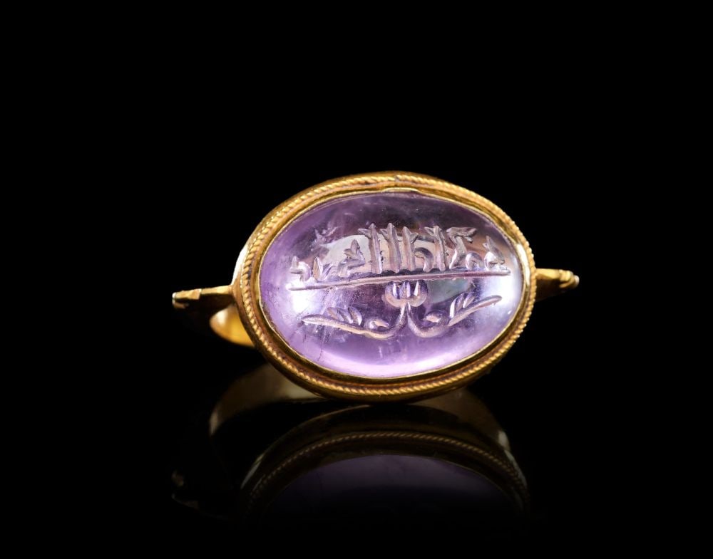 A CALLIGRAPHIC INSCRIBED AMETHYST RING ON GOLD, 14TH CENTURY AND LATER, PERSIA: A CALLIGRAPHIC INSCRIBED AMETHYST RING ON GOLD, 14TH CENTURY AND LATER, PERSIA The ring set with a substantial oval amethyst cabochon mounted horizontally in a closed gold bezel, the collet edged with