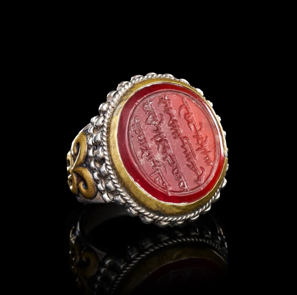 A CALLIGRAPHIC INSCRIBED CARNELIAN RING ON SILVER, 19TH CENTURY, PERSIA: A CALLIGRAPHIC INSCRIBED CARNELIAN RING ON SILVER, PERSIA, 19TH CENTURY Of substantial form, the oval carnelian bezel set within a plain gilt collar and framed by a double border of twisted silver wir
