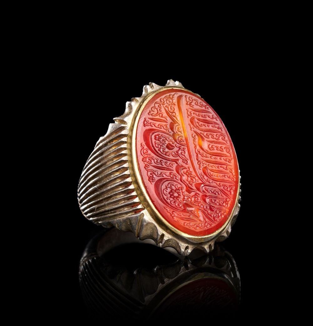 A CALLIGRAPHIC INSCRIBED AGATE RING ON SILVER, 19TH CENTURY, PERSIA: A CALLIGRAPHIC INSCRIBED AGATE RING ON SILVER, PERSIA, 19TH CENTURY The ring of substantial form, the shank rising in tightly ribbed silver flanks that terminate at the shoulders in raised serrated cr