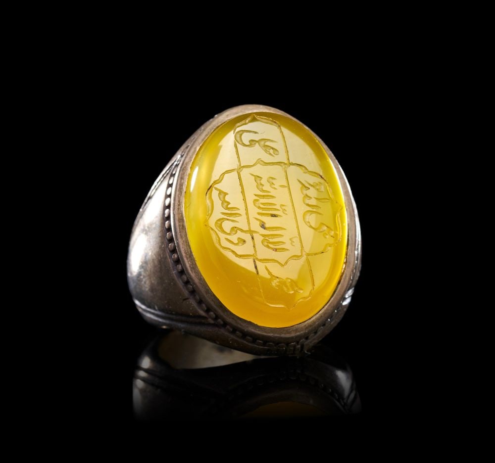 A CALLIGRAPHIC INSCRIBED AGATE RING ON SILVER, 19TH CENTURY, PERSIA: A CALLIGRAPHIC INSCRIBED AGATE RING ON SILVER, PERSIA, 19TH CENTURY The ring of substantial form, the silver hoop with tapering shoulders bordered by fine beaded mouldings and incised linear ornament,