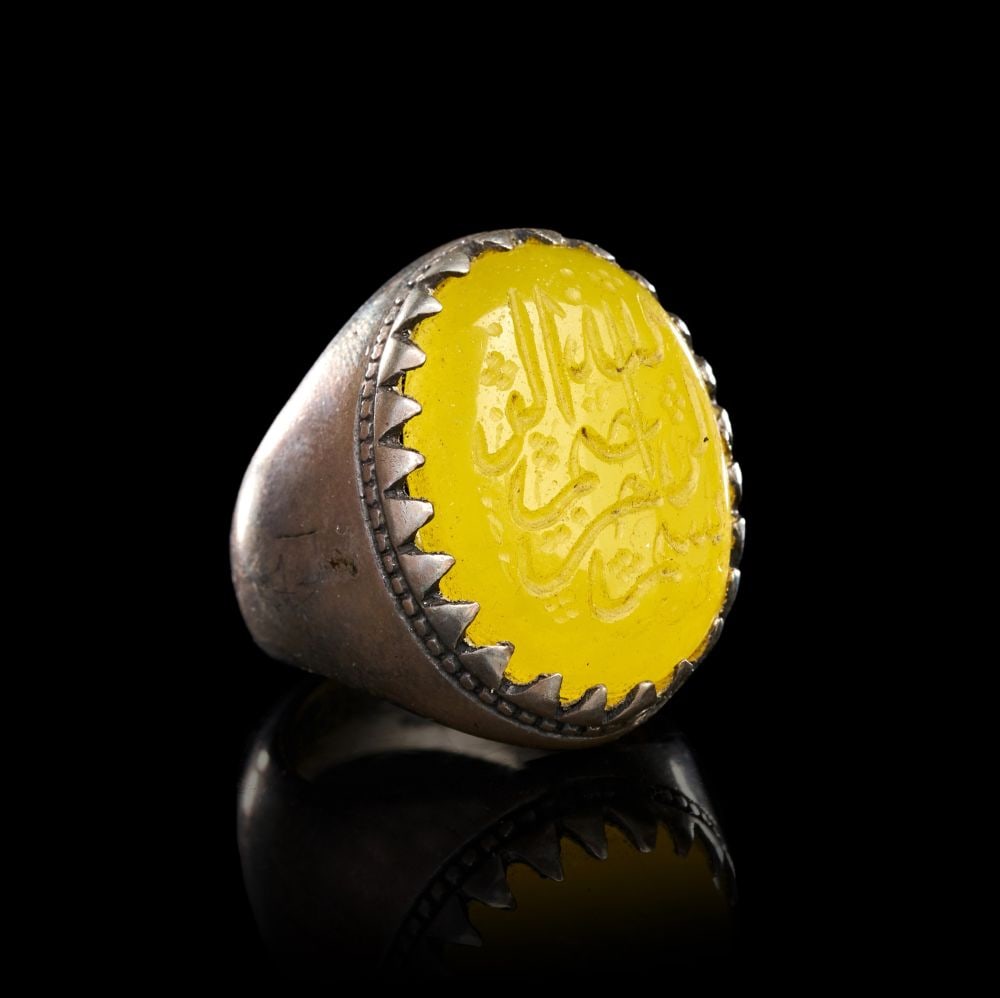 A CALLIGRAPHIC INSCRIBED AGATE RING ON SILVER, 19TH CENTURY, PERSIA: A CALLIGRAPHIC INSCRIBED AGATE RING ON SILVER, PERSIA, 19TH CENTURY The ring of substantial form, the tapering silver shank rising to a broad oval bezel set with a domed yellow agate cabochon. The sto