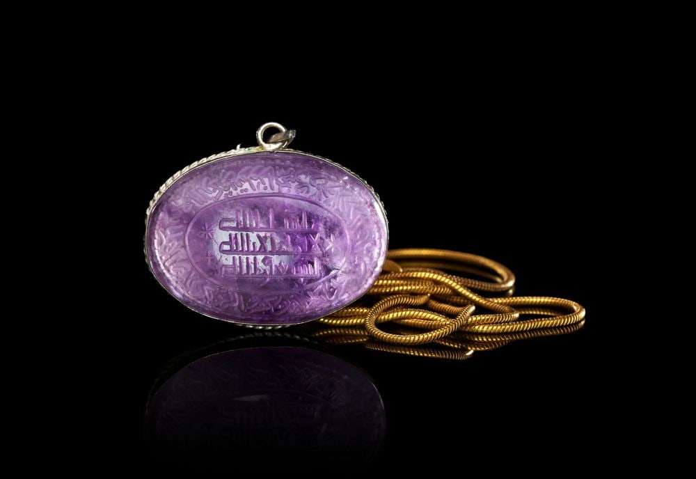 A CALLIGRAPHIC INSCRIBED AMETHYST AMULET, 19TH CENTURY, PERSIA: A CALLIGRAPHIC INSCRIBED AMETHYST AMULET, PERSIA, 19TH CENTURY Of oval form, the translucent amethyst cabochon carved in intaglio on its upper face with a central cartouche of Arabic inscription in mi