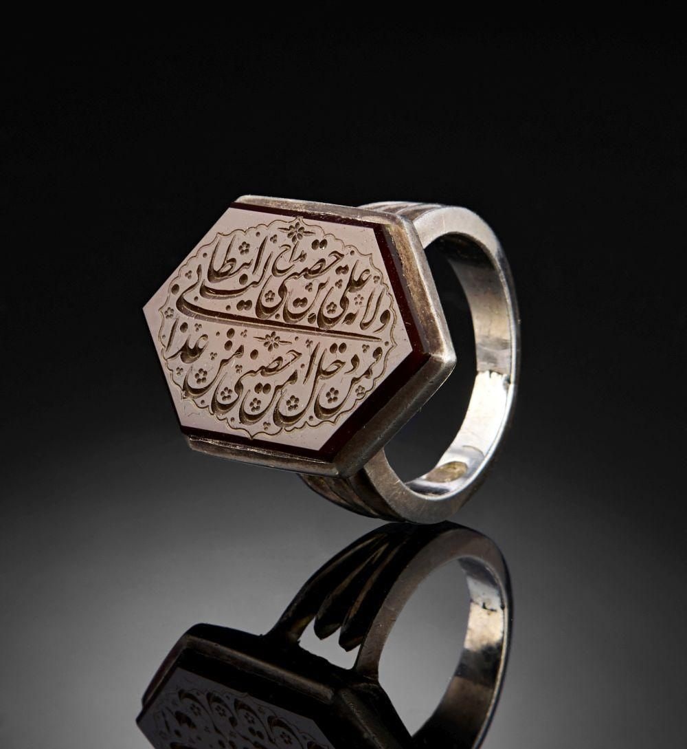 A CALLIGRAPHIC INSCRIBED AGATE RING, 19TH CENTURY, PERSIA: A CALLIGRAPHIC INSCRIBED AGATE RING, PERSIA, 19TH CENTURY The hexagonal carnelian-agate bezel is set within a heavy silver mount, the shoulders rising in stepped bands to enclose the stone in a plain 