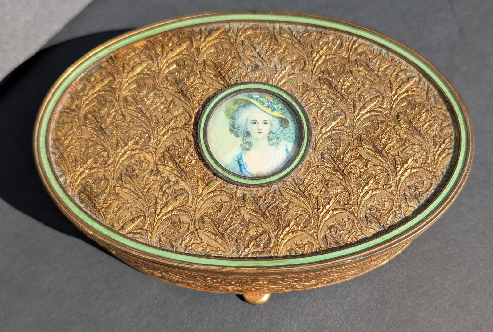 Vintage Apollo Gilt Brass Jewelry/Trinket Box w/Miniature Painting.: Vintage Apollo Gilt Brass Jewelry/Trinket Box with Painted Miniature of a Young Woman on the Top. Stylized overall engraving with Green Enamel Band. On 4 bun feet. Stamped Apollo on the bottom. Origin