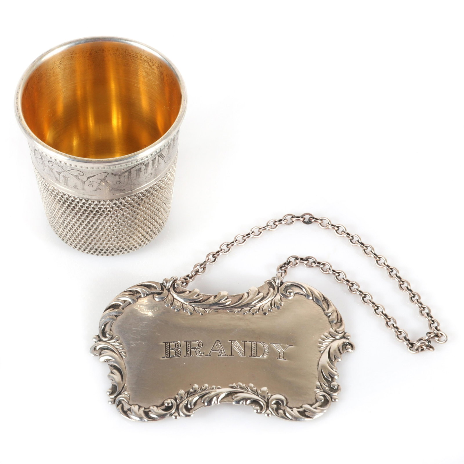 Antique sterling silver barware 2pc.; figural shot: Antique sterling silver barware 2pc.; figural shot glass novelty with vermeil interior, 'Just a Thimble full", and a Brandy decanter tag. 1 3/4"H x 1 3/4" diam