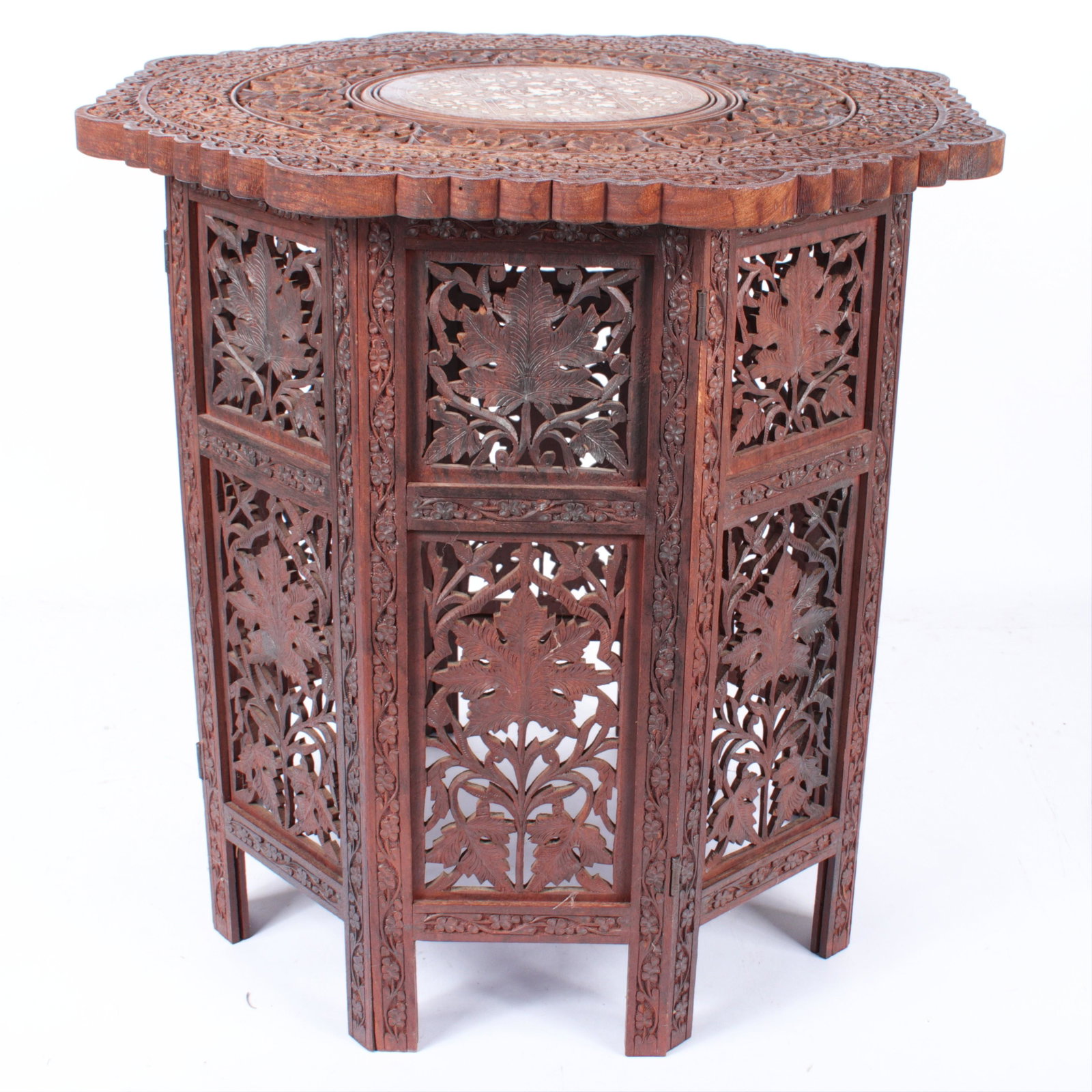 Indo Persian carved octagonal folding table with hinged: Indo Persian carved octagonal folding table with hinged panels and removable top. Profusely carved floral panels with central inlay roundel on top. 21 1/4"H x 22W