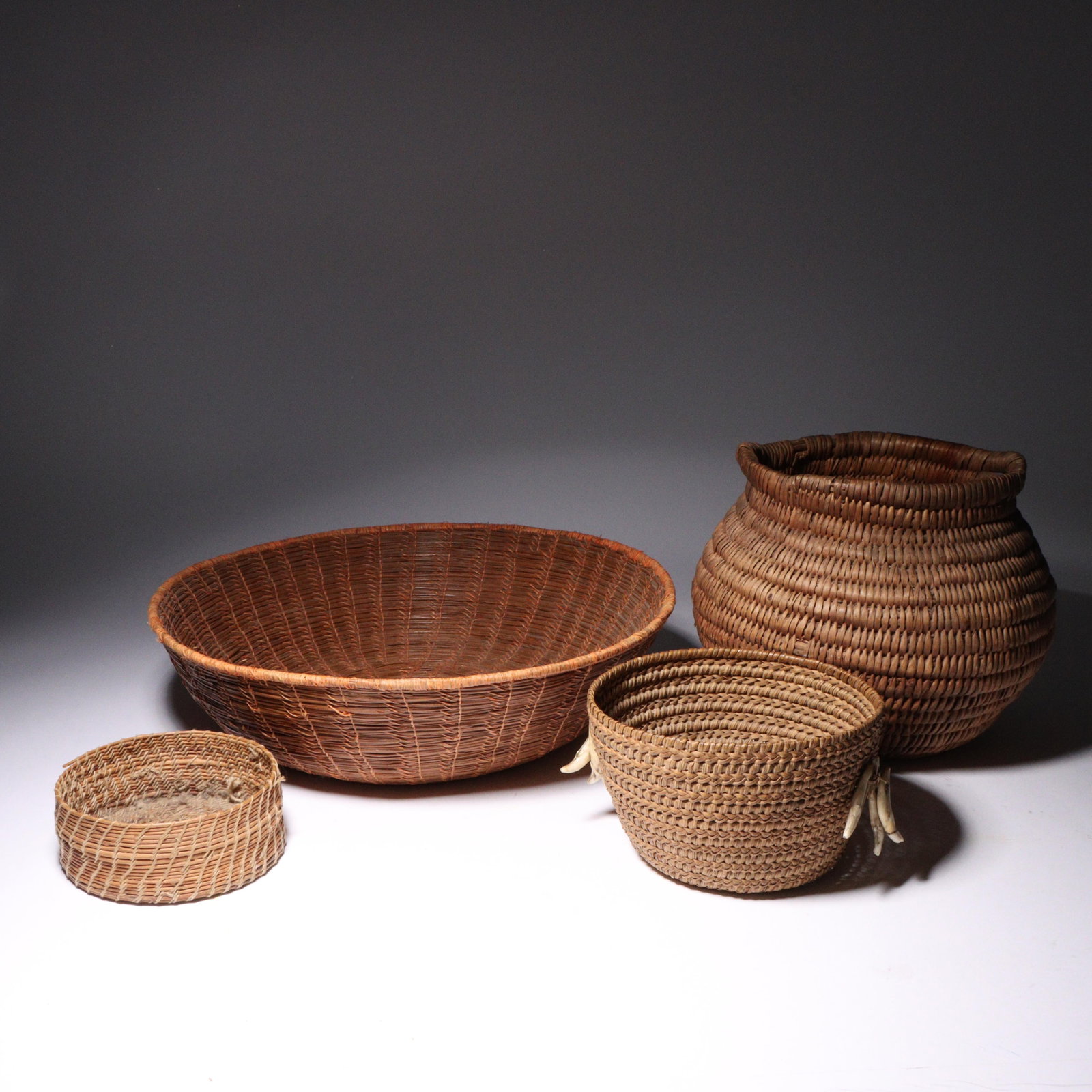 Native American basketry, 4pc: includes double handled coil basket, pine needle baskets, and one: Native American basketry, 4pc: includes double handled coil basket, pine needle baskets, and one adorned with teeth 3 1/4"H x 12" diam. (largest)
