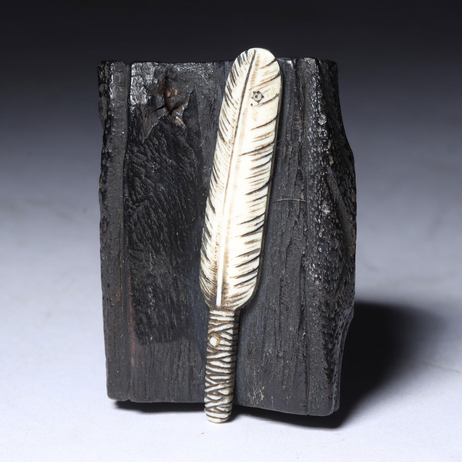 Antique carved black wood netsuke in form of split log with white carved bone feather lying on top,: Antique carved black wood netsuke in form of split log with white carved bone feather lying on top, inset signature in red, detailed bark texture with knot hole on log 1 3/4"H x 1 1/4"W