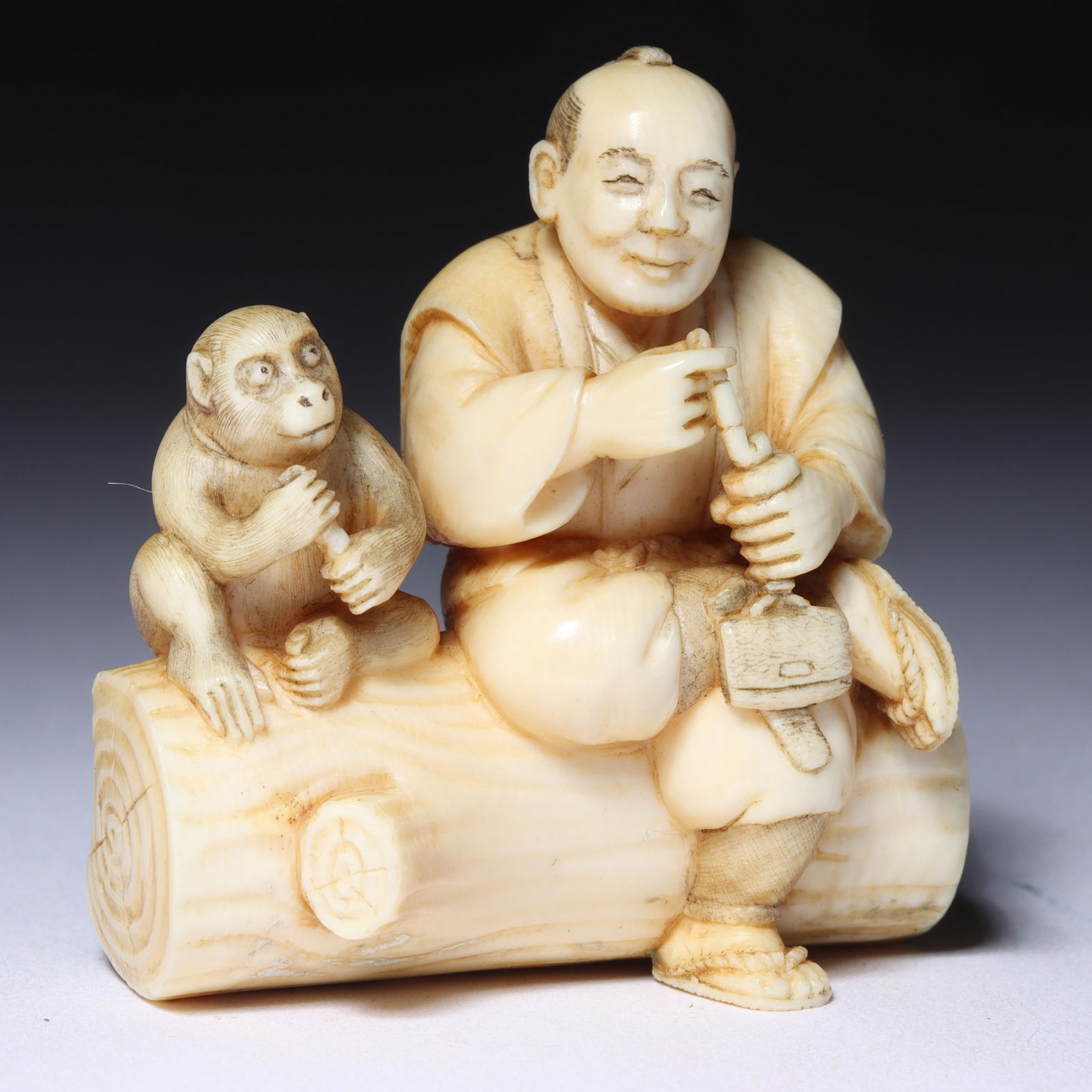 Japanese carved netsuke; man and monkey seated on log with pip and tobacco bag, red inset seal (1 of 8)