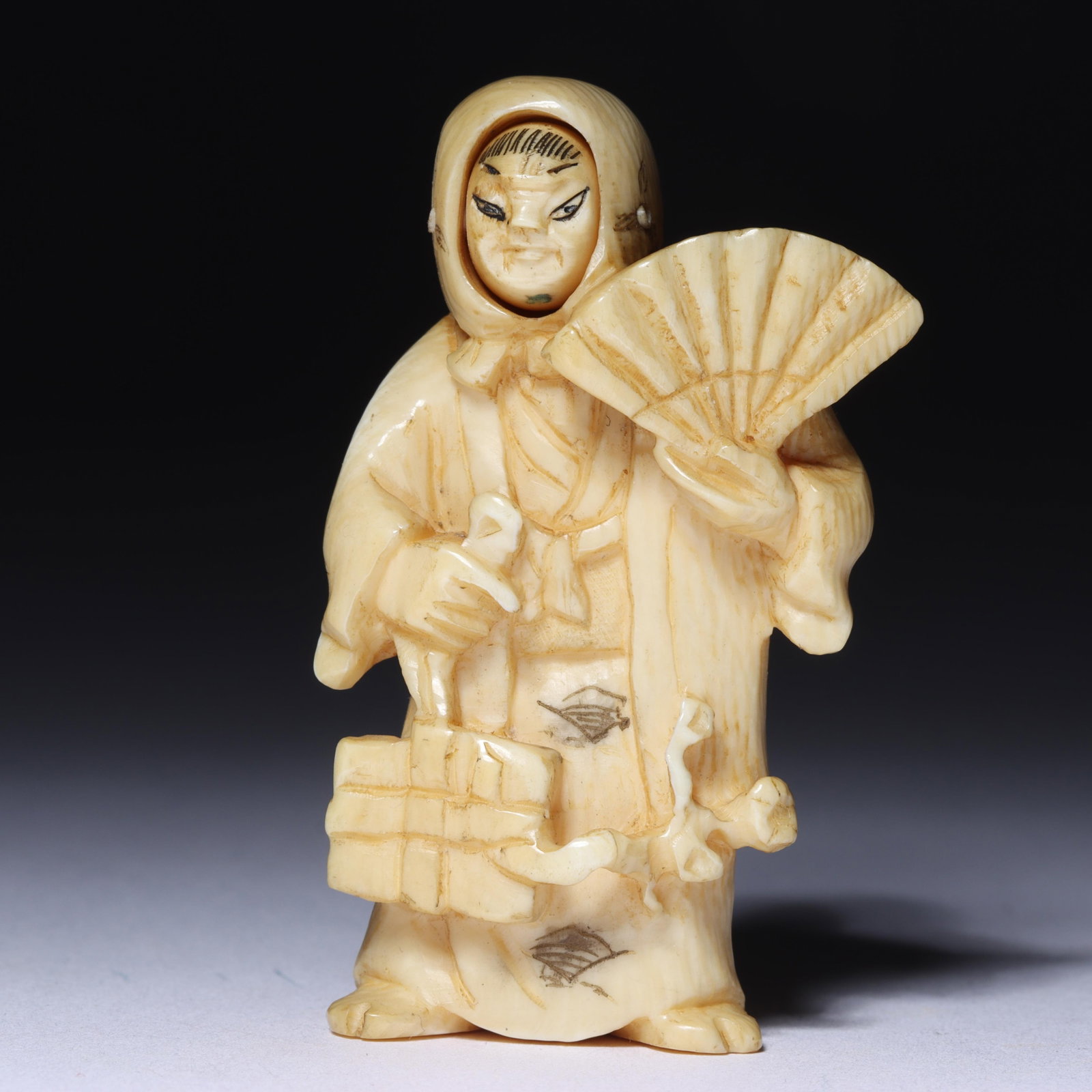 Japanese carved bone figural mechanical netsuke: kabuki actor holding a fan carrying a package and a: Japanese carved bone figural mechanical netsuke: kabuki actor holding a fan carrying a package and a ribbon, revolving face, signed by artist. 2"H x 1 1/2"W