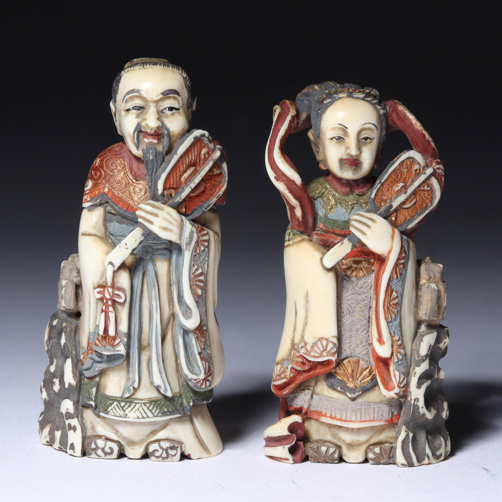 Pair Japanese carved bone figural netsuke; polychrome and gilt hand painted court couple, man and: Pair Japanese carved bone figural netsuke; polychrome and gilt hand painted court couple, man and woman noble figures holding fans, signed. hand painted robes of black, red and gold leaf, incensor at 