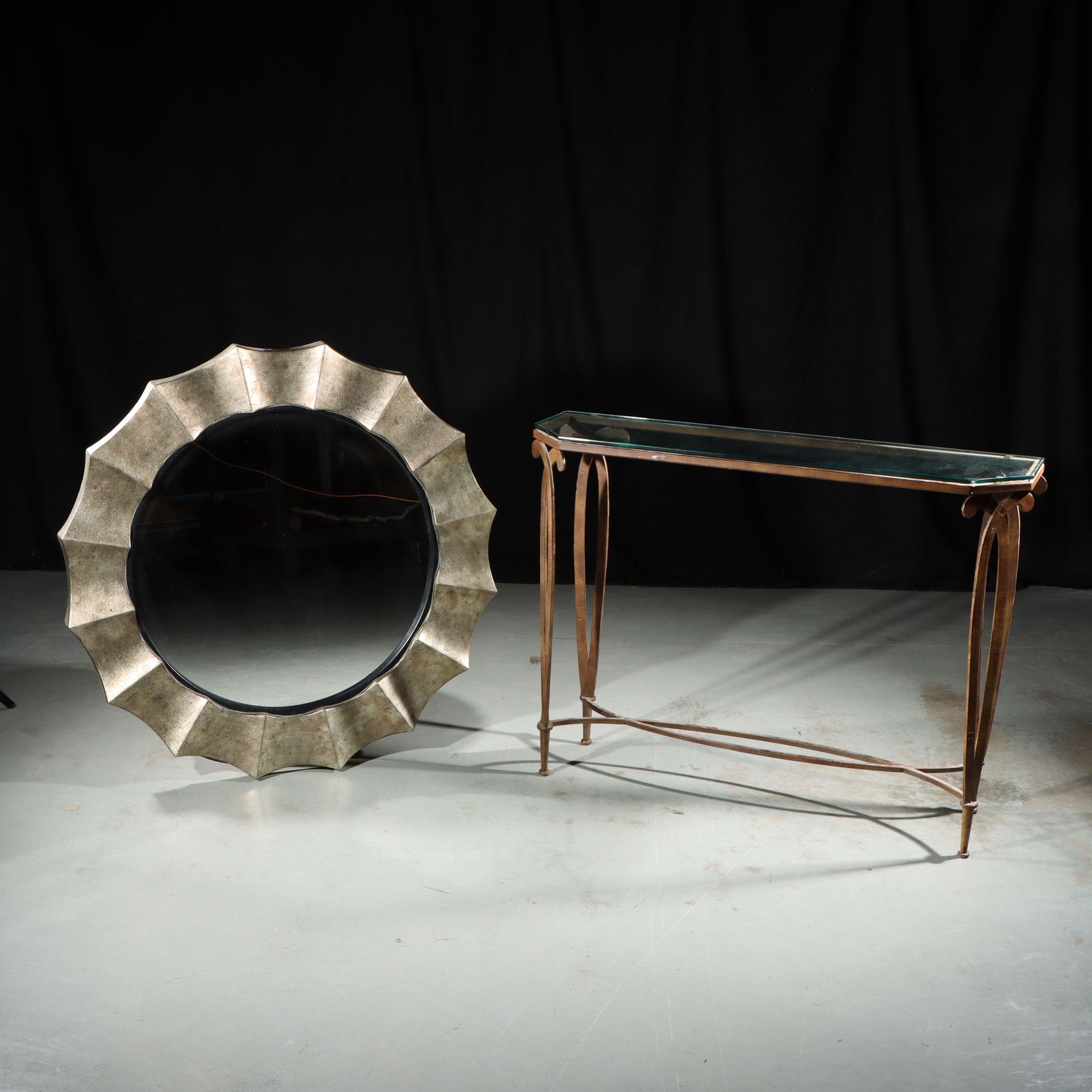 Uttermost 'Gotham' antiqued metallic round wall mirror and metal and glass console table with rustic: Uttermost "Gotham" antiqued metallic round wall mirror and metal and glass console table with rustic finish Glass on console table is chipped. 33 3/4"H x 45 1/2"W (table)