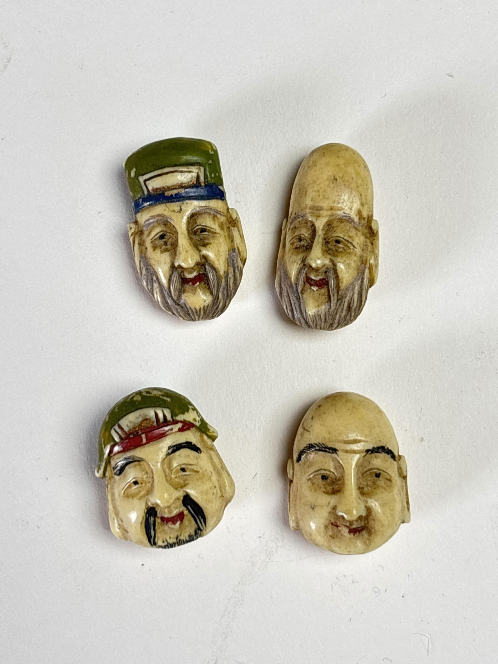 Lot of 4 antiqued carved and painted Asian man head pennants, possibly carved in bone, back roughly: Lot of 4 antiqued carved and painted Asian man head pennants, possibly carved in bone, back roughly translates to ?common people?? 1?H each
