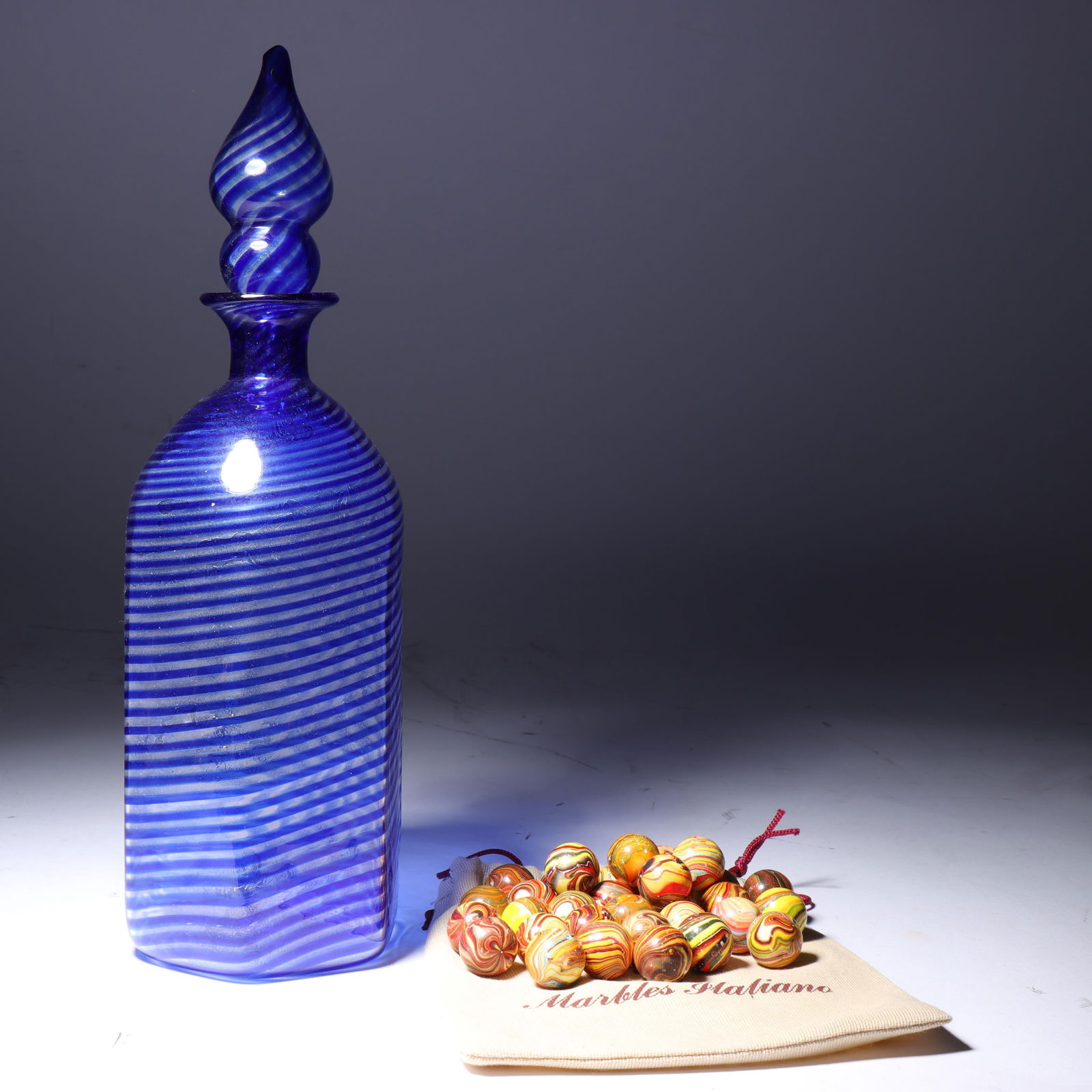 Murano art glass decanter bottle and Italian art glass Marbles Italiano. 12"H x 4 1/4"W (bottle): Murano art glass decanter bottle and Italian art glass Marbles Italiano. Marbles in a bag marked Made in Italy for Cavallini & Co. San Francisco. 12"H x 4 1/4"W (bottle)