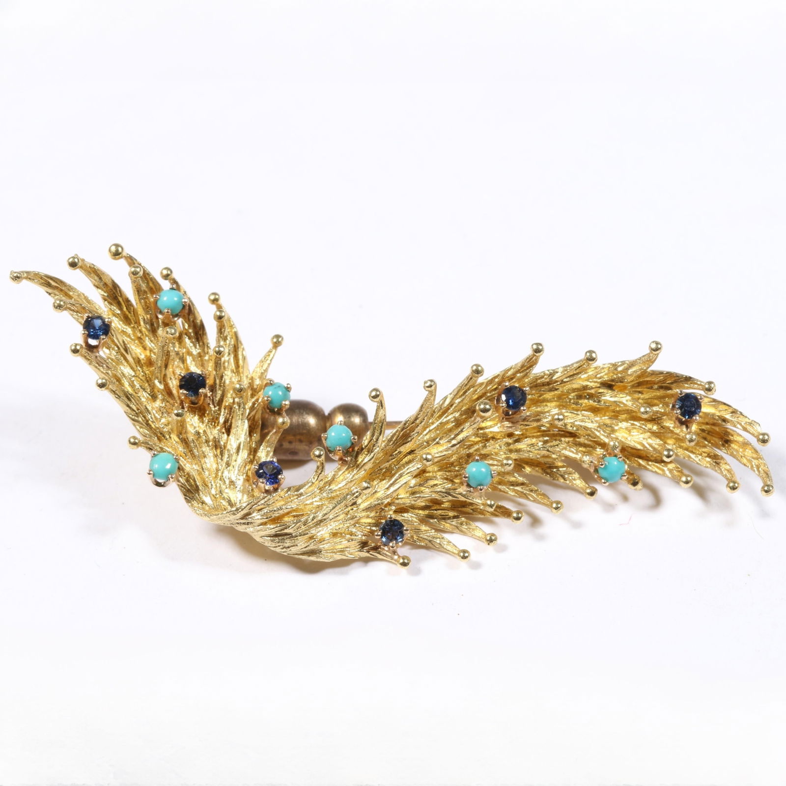 18K yellow gold feathered brooch with turquoise and sapphire accents. 2 3/4"L x 1 1/4"W: 18K yellow gold feathered brooch with turquoise and sapphire accents. Pin guard is NOT gold. 8.861DWT (without pin guard) The purchase of gold requires confirmed funds. 2 3/4"L x 1 1/4"W