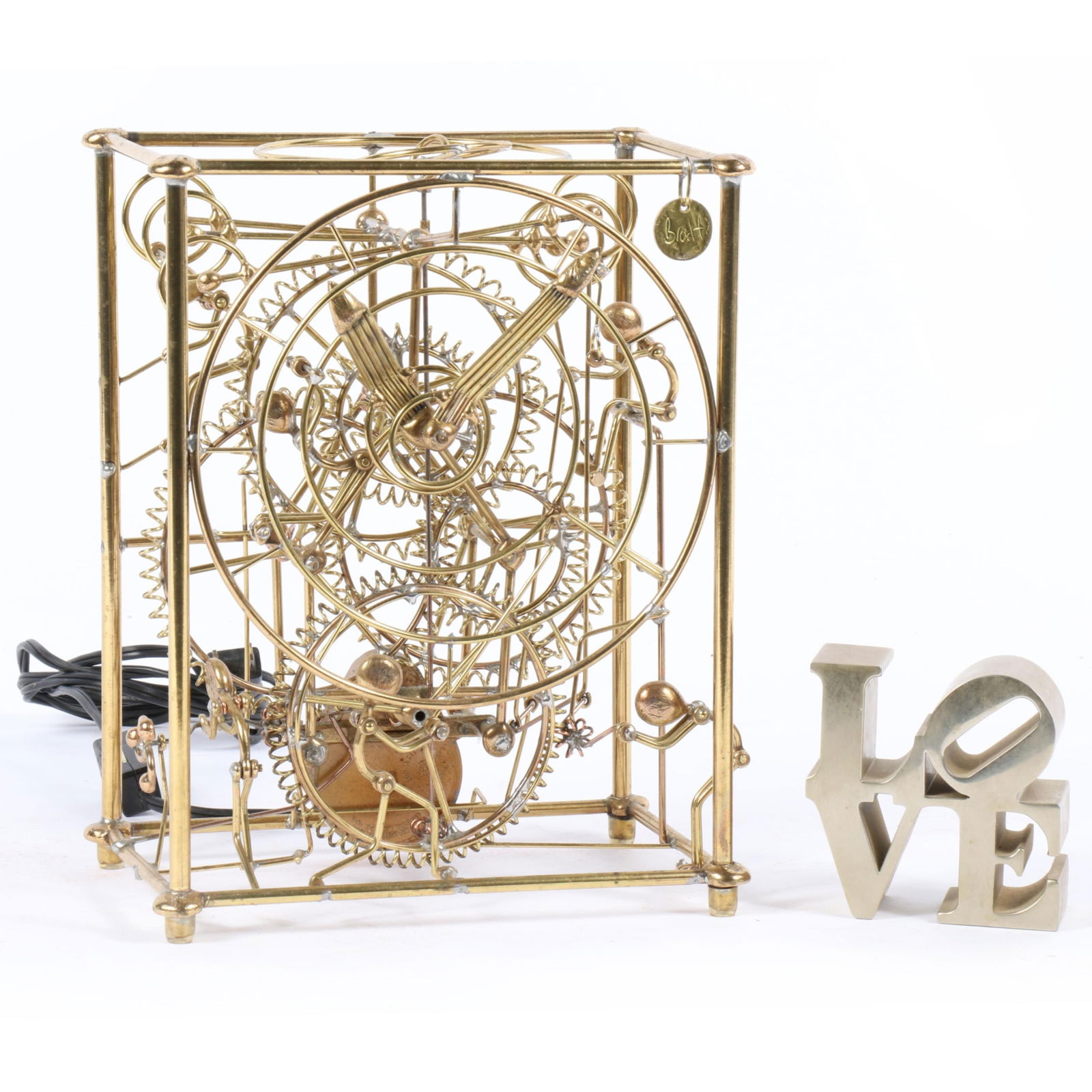 Gordon Bradt (1924-2022) Kinetico Studios Six Man electric kinetic brass sculpture clock and Robert: Gordon Bradt (1924-2022) Kinetico Studios Six Man electric kinetic brass sculpture clock and Robert Indiana LOVE metal sculpture paperweight. 9 1/4"h x 7 1/4" W x 4 5/8" D (clock)