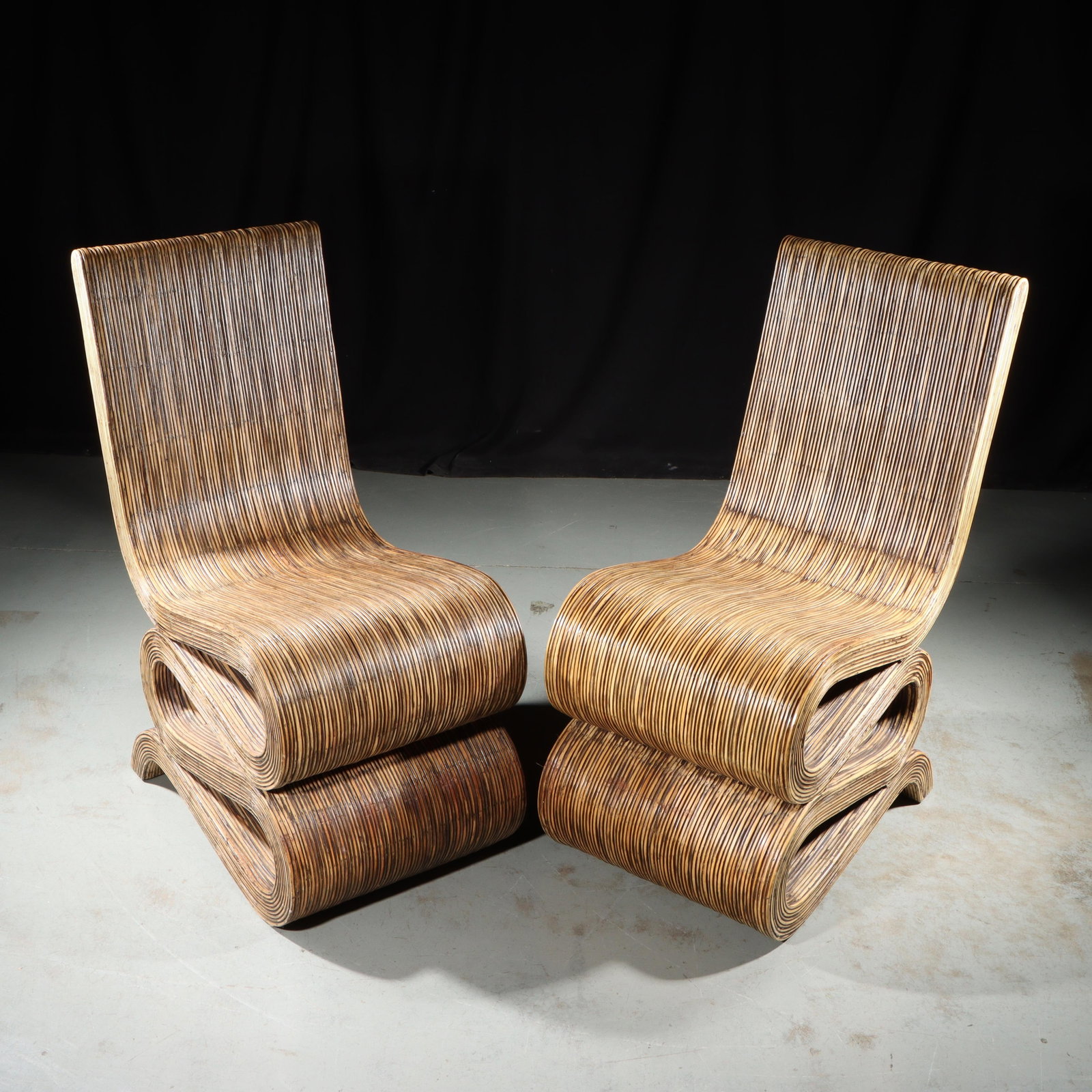 Pair modern contemporary pencil rattan snake chairs in the style of Frank Gehry. 35 1/2"H x 16 1/4"W: Pair modern contemporary pencil rattan snake chairs in the style of Frank Gehry. A pair of vintage pencil reed lounge chairs featuring a distinctive curved design. The chairs are constructed with bamb