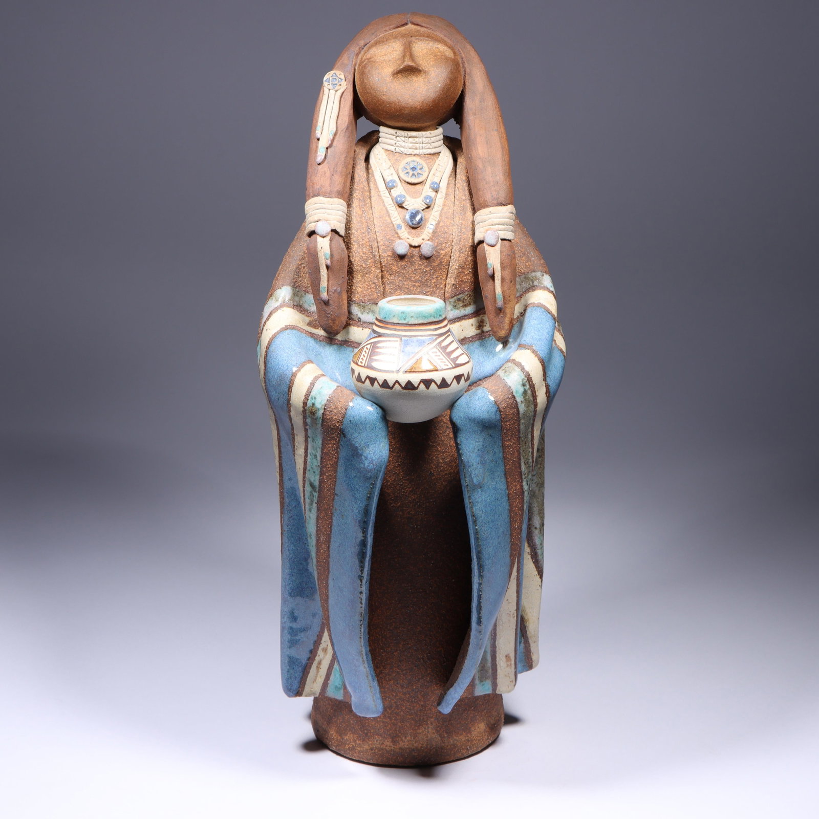 Terry L. Slonaker Native American "Plains Woman with Pot" figural pottery sculpture, 1988, 15 1/2"H: Terry L. Slonaker Native American "Plains Woman with Pot" figural pottery sculpture, 1988 Incised signature and date on base. Numbered 967. Pottery on left pigtail is loose. Provenance: purchased from