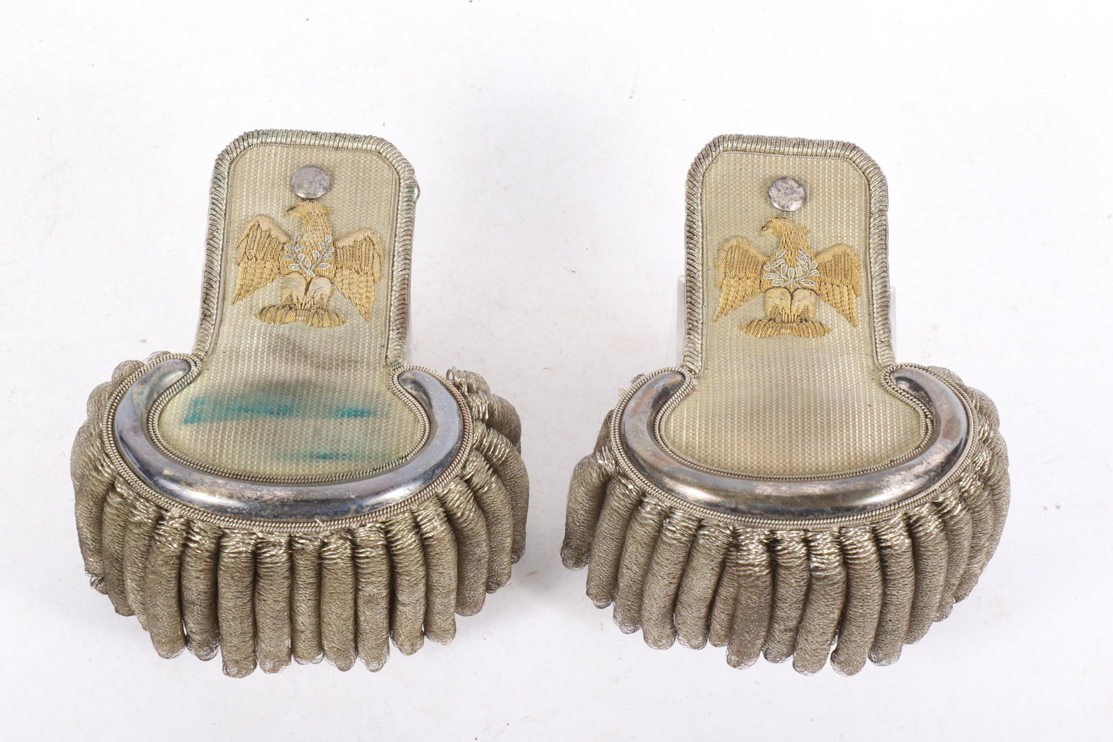 Pair US Colonel epaulets with silver bullion fringe and embroidered eagle insignia 4"D x 6"W x 7"D: Pair US Colonel epaulets with silver bullion fringe and embroidered eagle insignia A pair of US military colonel epaulets featuring gold embroidery with an eagle emblem. These epaulets are typically u