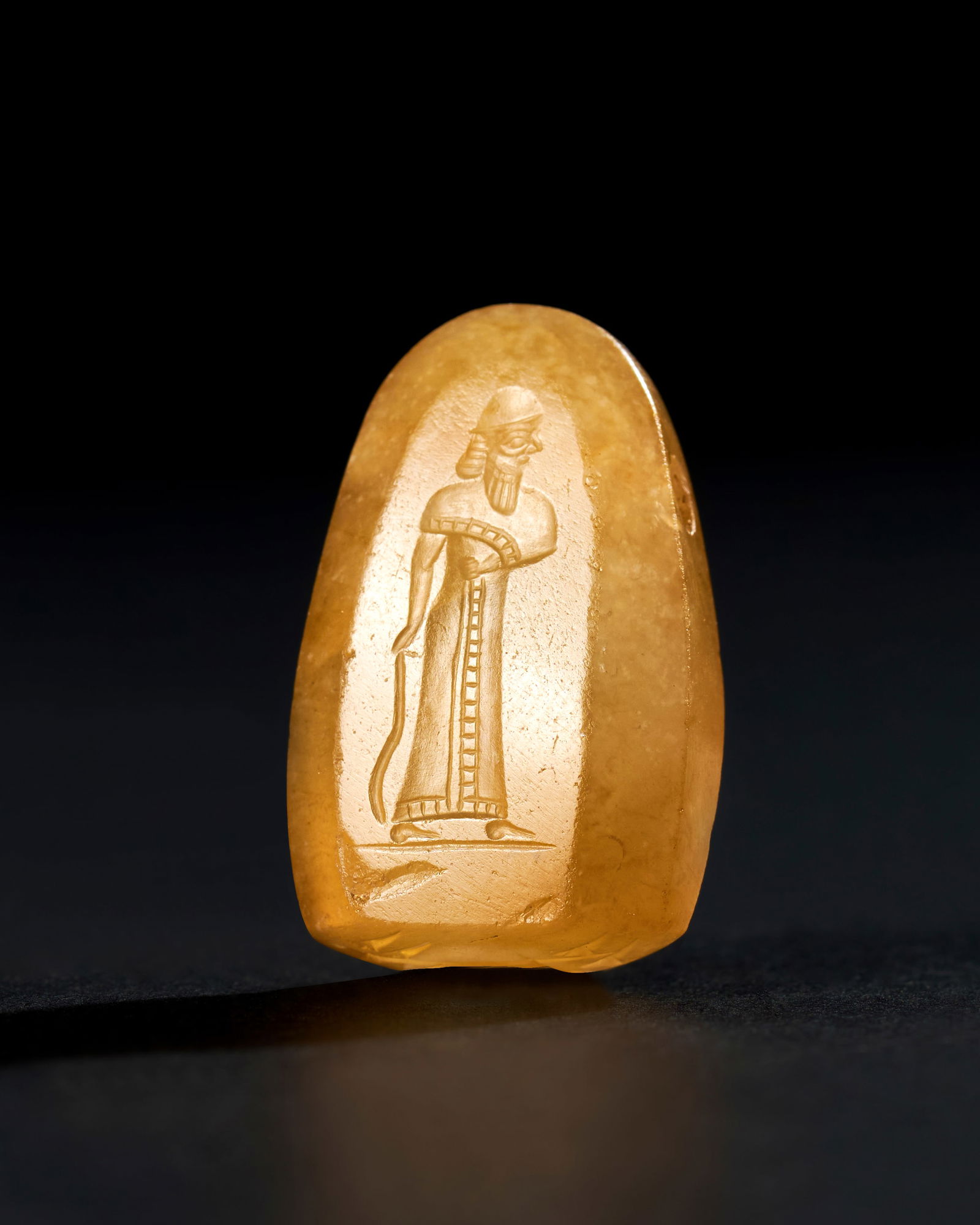 A NEO BABYLONIAN AGATE STAMP SEAL, CIRCA 700 - 600 B.C.: This exquisite Neo-Babylonian stamp seal, carved from a beautifully translucent agate, dates back to circa 700 - 600 B.C. The seal features a finely detailed engraving of a standing figure, dressed in