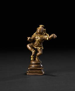 A RARE SOUTH INDIAN TANJORE BRASS INLAID BRONZE FIGURE OF KRISHNA, 18TH CENTURY: The youthful form of Krishna is captured mid-step, with one leg raised and arms gracefully extended in rhythmic motion, embodying divine playfulness and grace. He wears a traditional tiered crown and